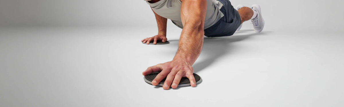 Close-up of hands on gray textured EQYP disc sliders during a plank exercise on the floor.