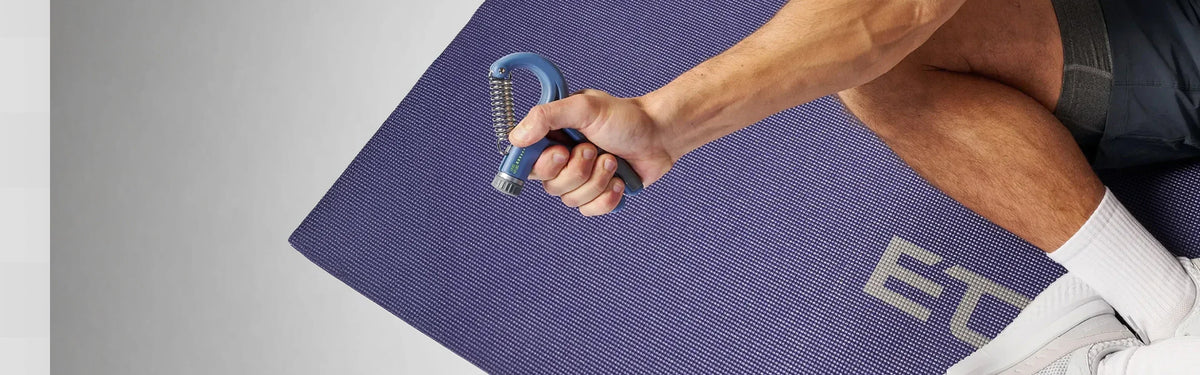 Close-up of a hand squeezing a blue EQYP adjustable hand grip strengthener while kneeling on a EQYP yoga mat.