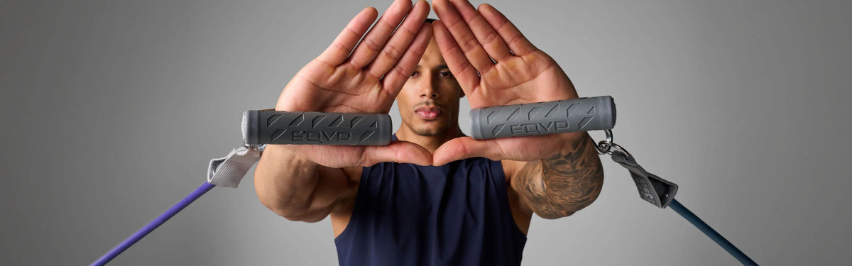 Man holding two gray EQYP resistance band handles with anchor straps extended outward, forming a triangle shape with his hands.