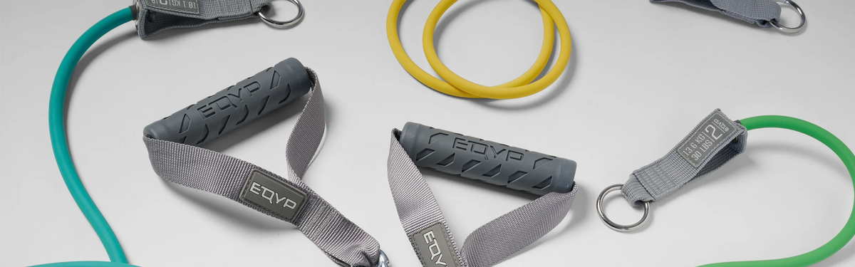 Flat lay of assorted EQYP resistance bands and tube handles in yellow, teal, and green, showing a strength training kit.