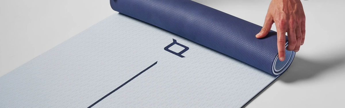Hand unrolling a navy and light blue EQYP Dual Layer Yoga Mat on the floor