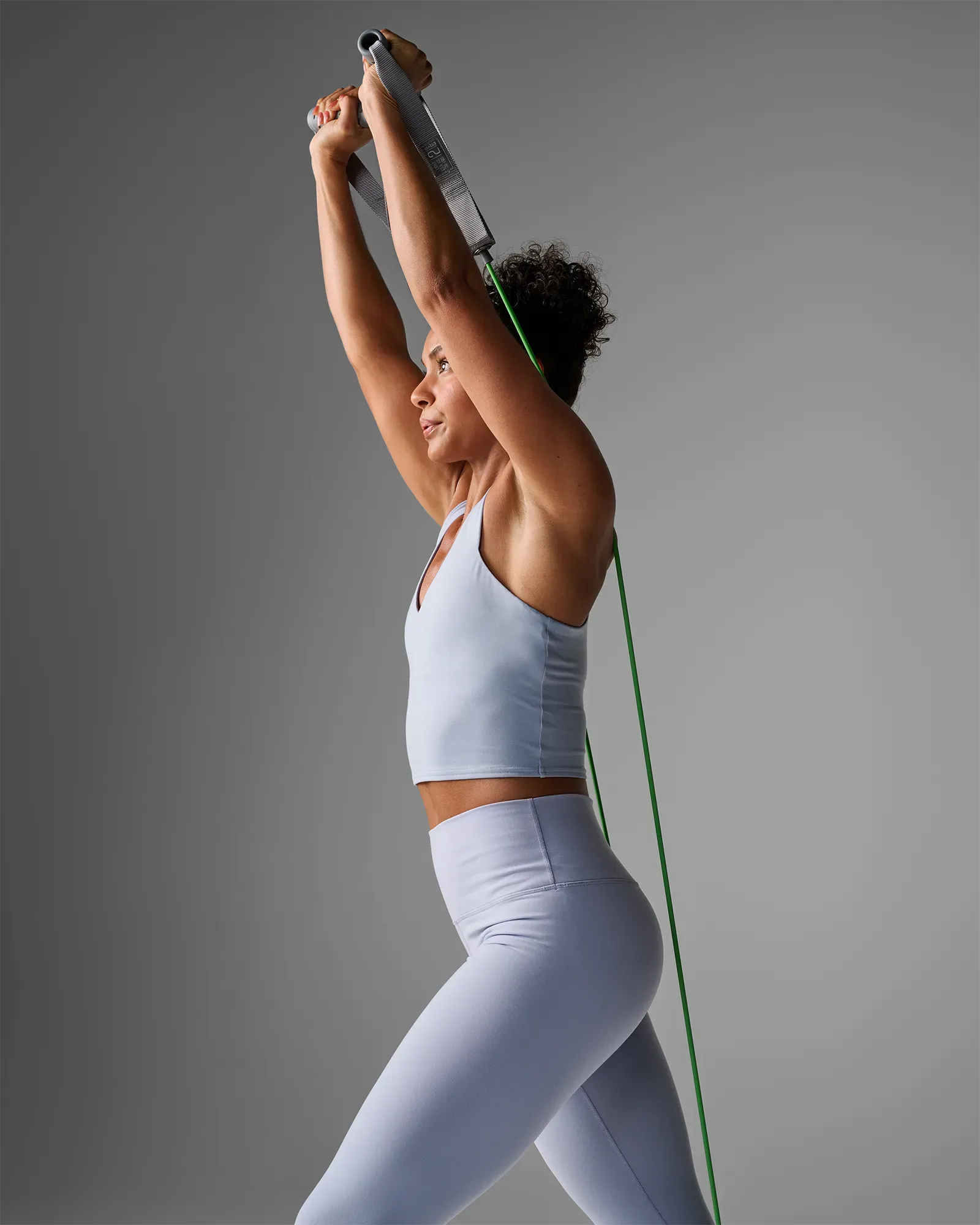 Woman performing a standing double-arm overhead press using EQYP Power Tubes with Handles light green resistance tube
