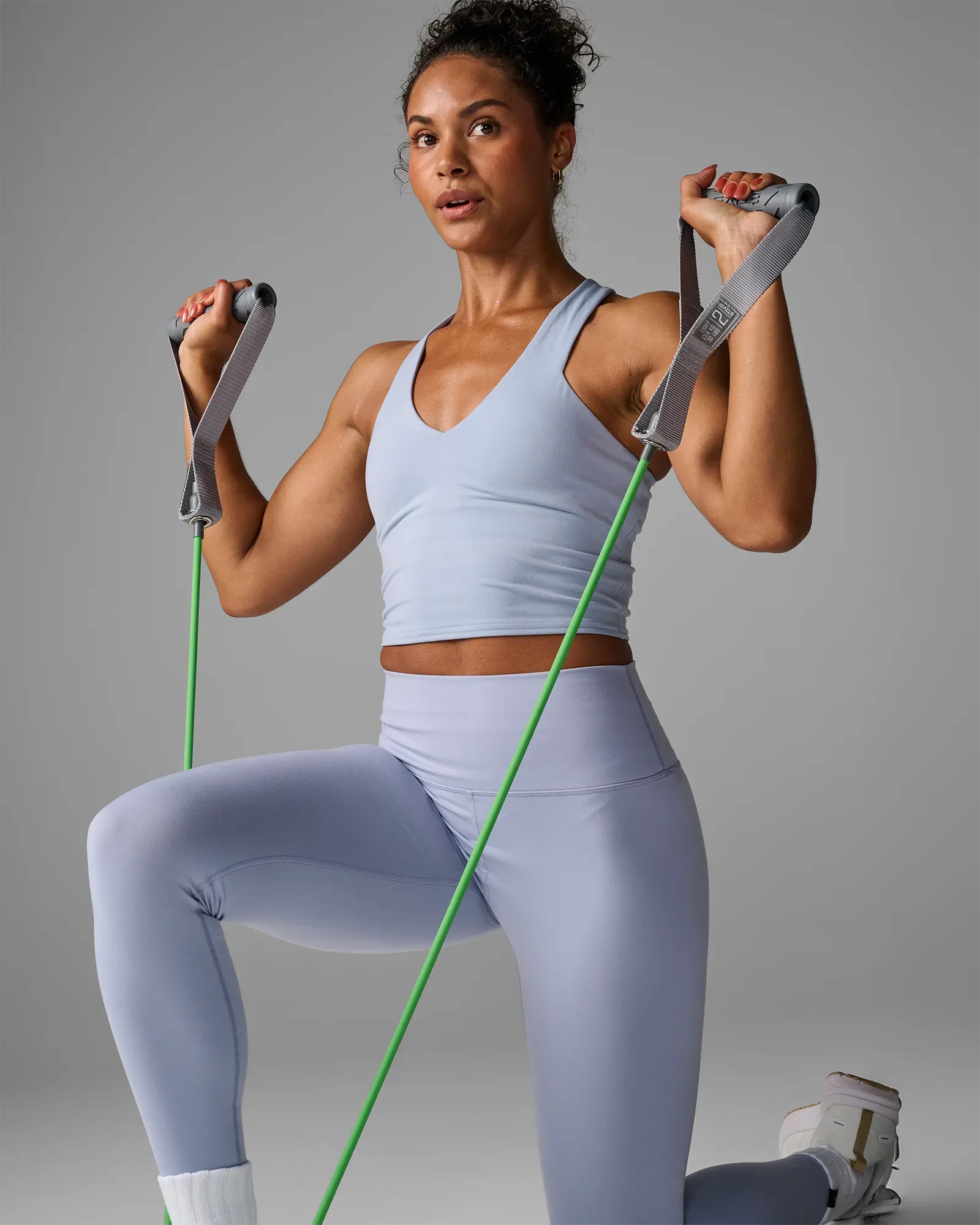 Woman performing a kneeling double-arm overhead press using EQYP Power Tubes with Handles Light green resistance tube