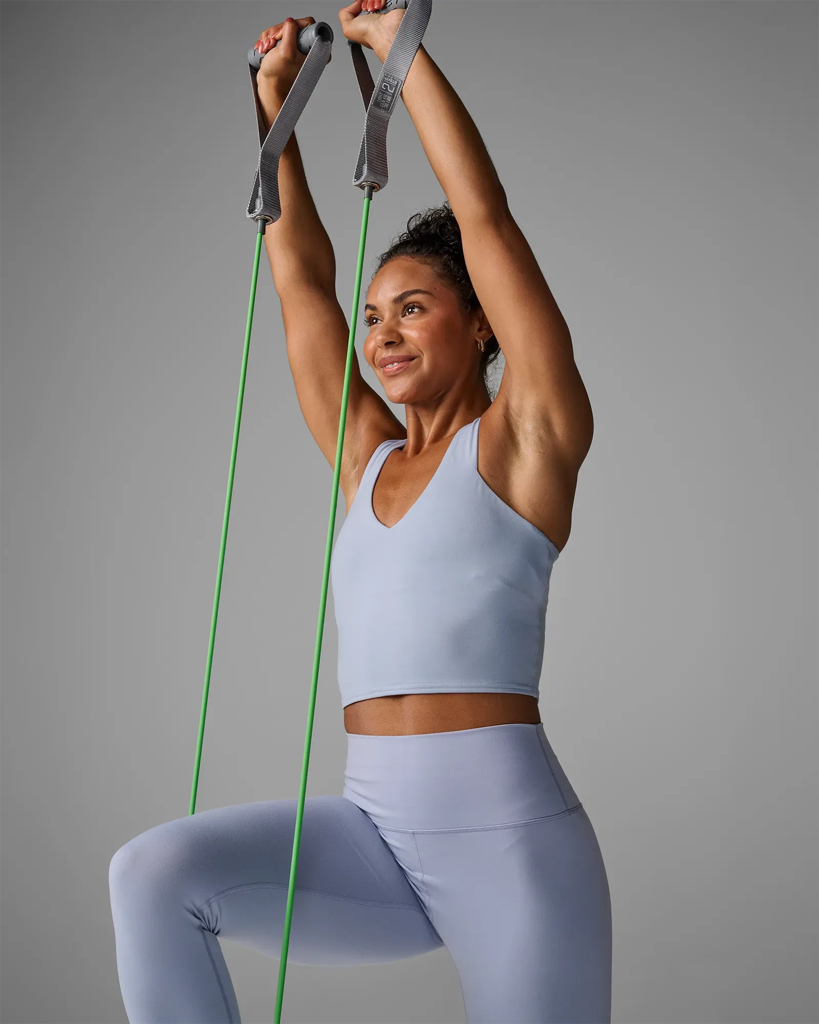 Woman performing a kneeling double-arm front raise using EQYP Power Tubes with Handles Light green resistance tube
