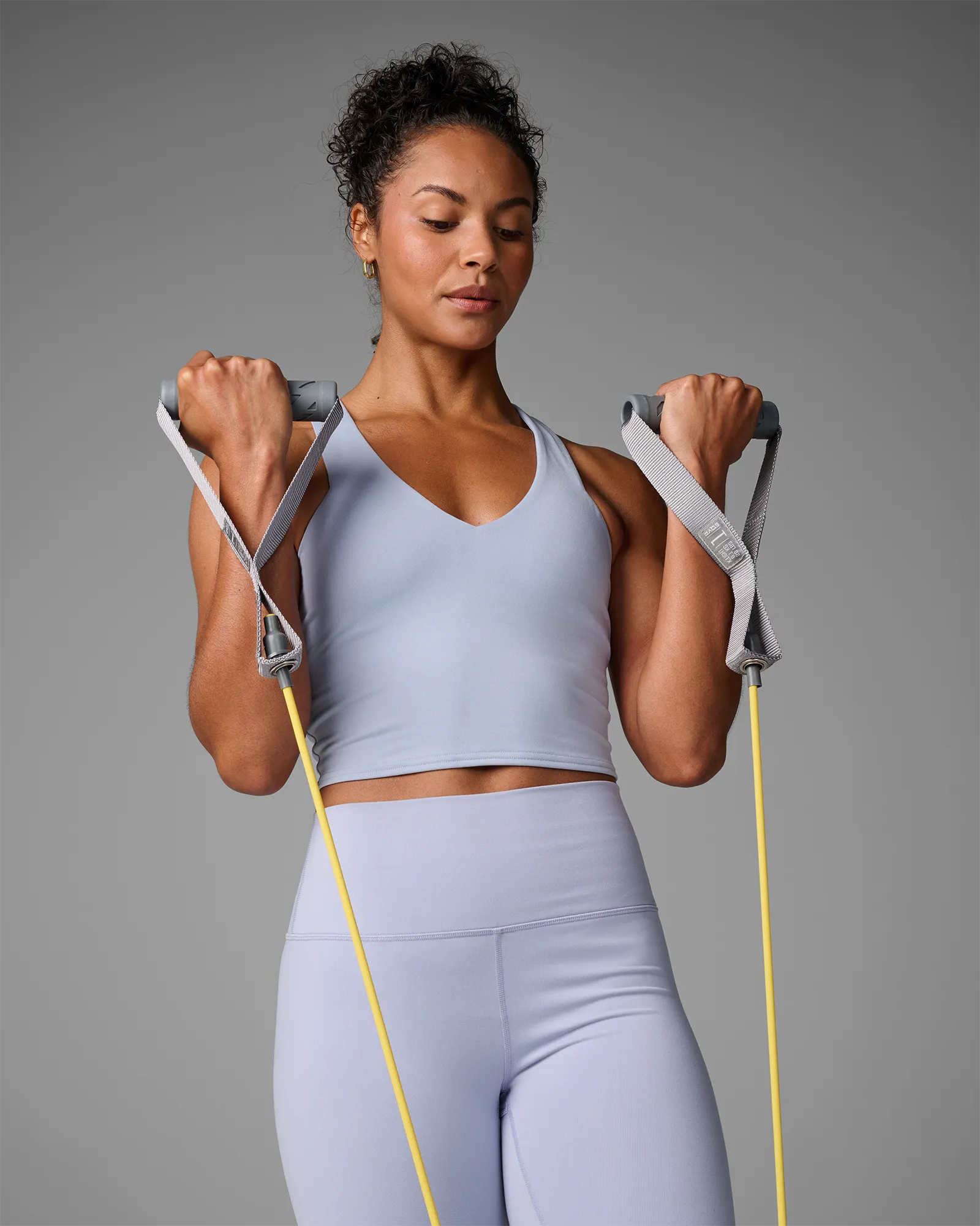 Woman performing a standing bilateral bicep curl using EQYP Power Tubes with Handles yellow resistance tube