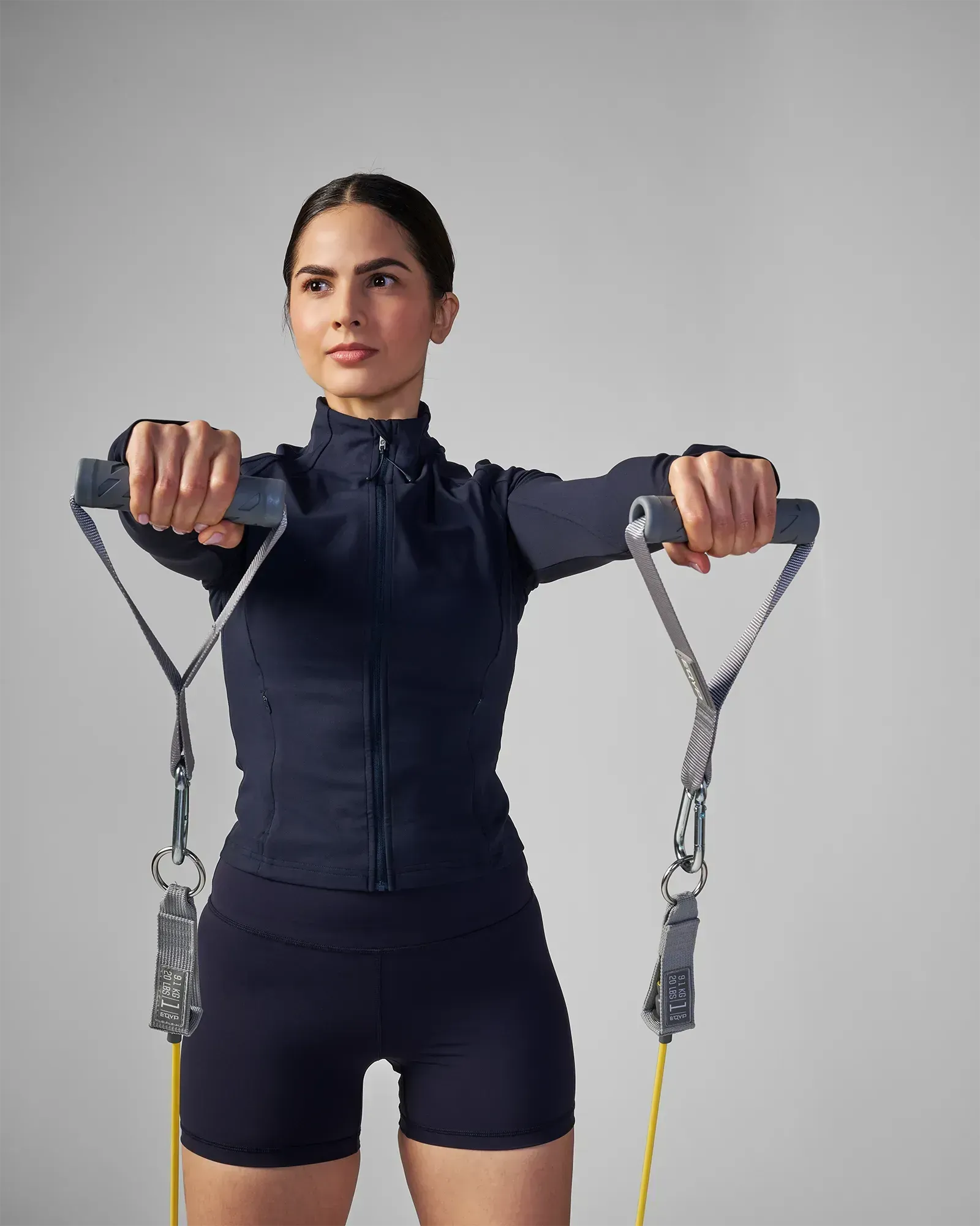 Woman performing a standing bilateral front lateral raise using EQYP Power Tubes 20 lbs yellow resistance tube with handles, front view