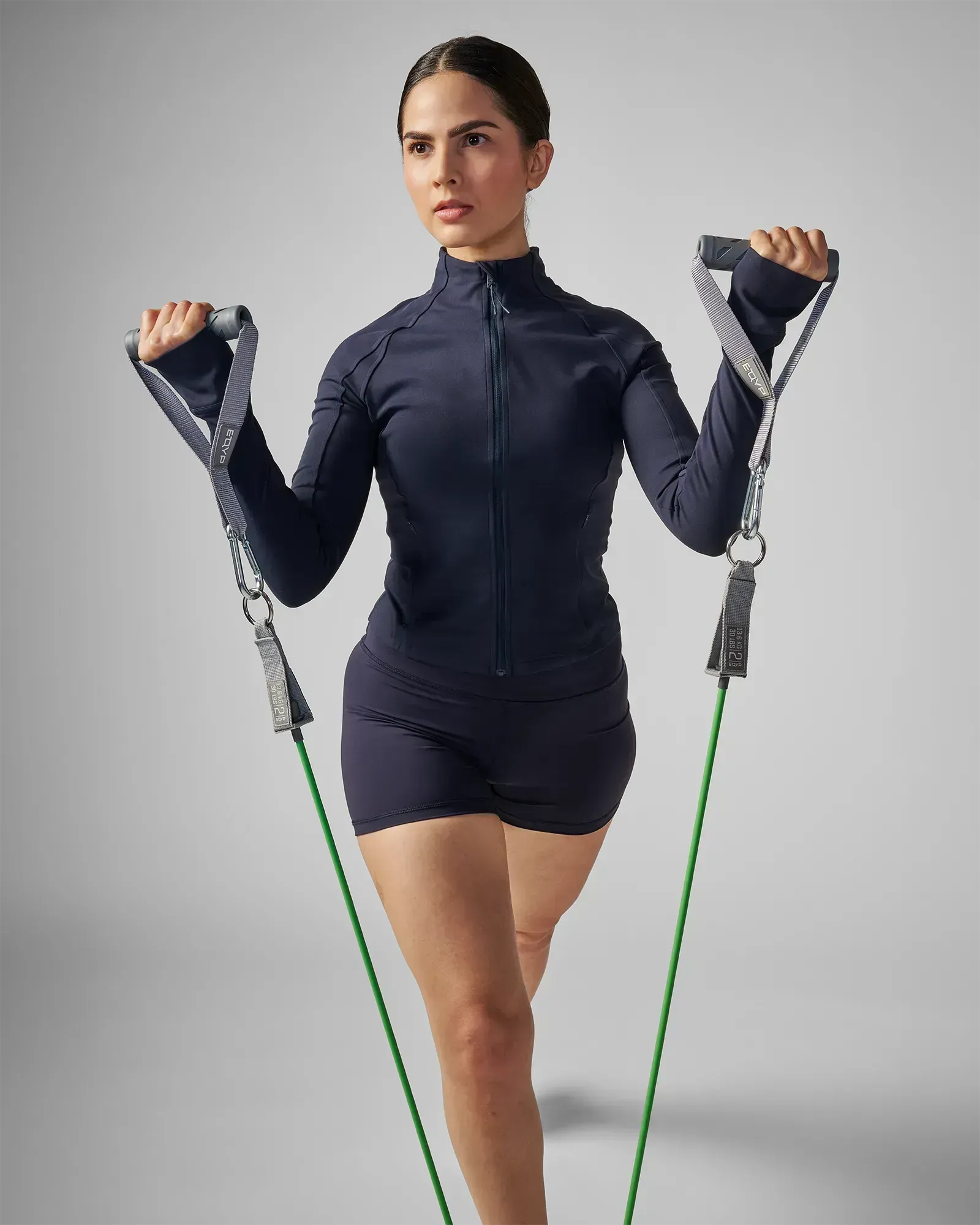 Woman performing a standing staggered bilateral bicep curl using EQYP Power Tubes 30 lbs green resistance tube with handles, front view