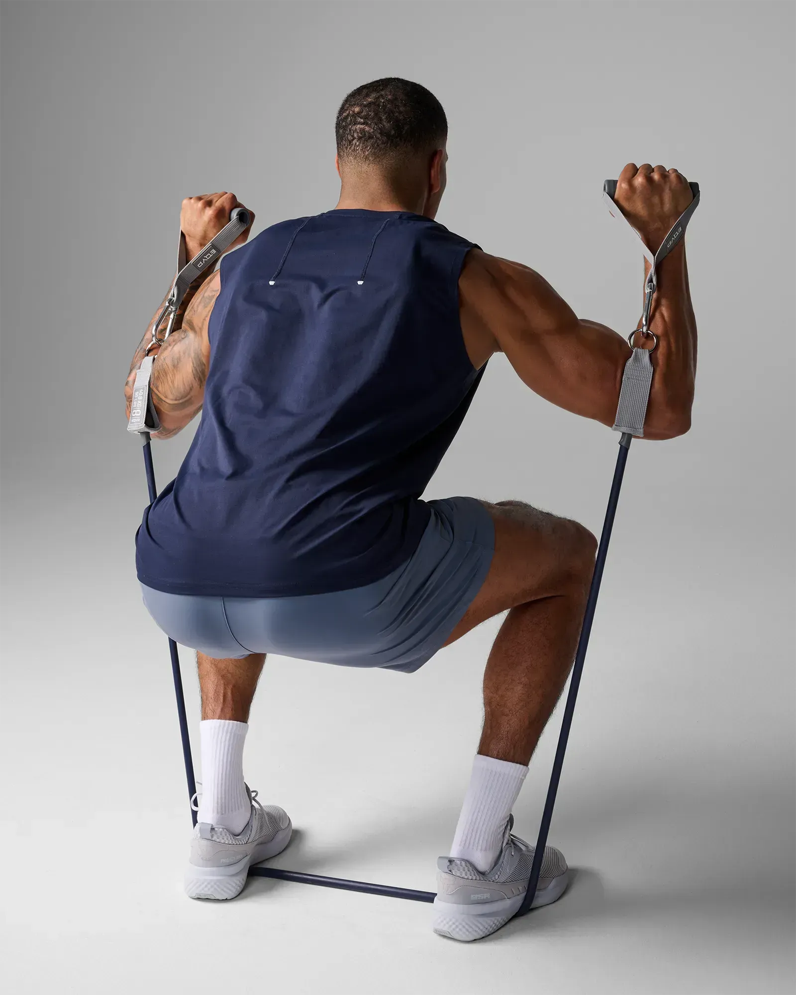 Man performing a squatting bilateral overhead press using EQYP Power Tubes 90 lbs navy blue resistance tube with handles, rear view