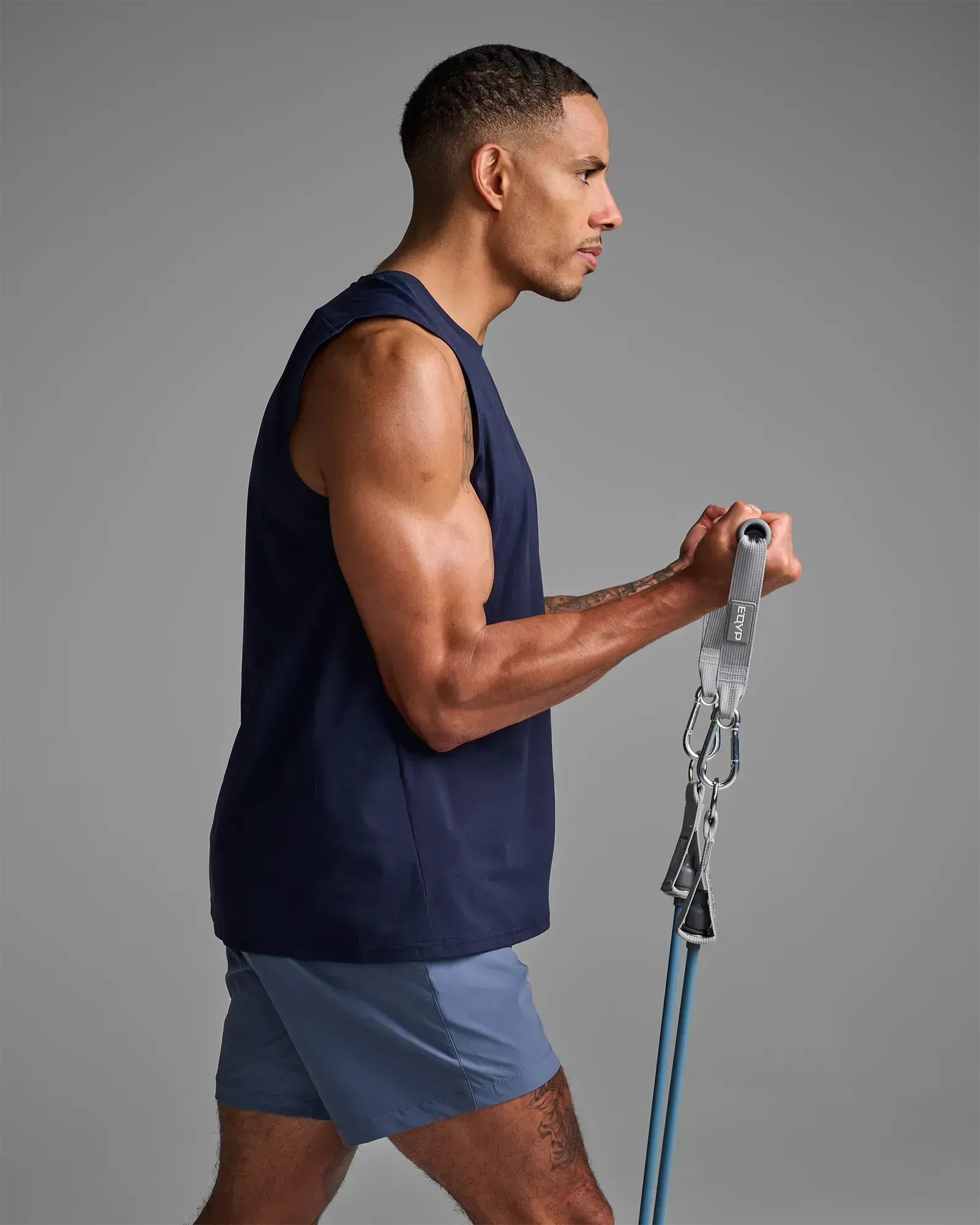 Man performing a standing unilateral bicep curl using EQYP Power Tube 70 lbs blue resistance tube with gray handle and carabiner clip