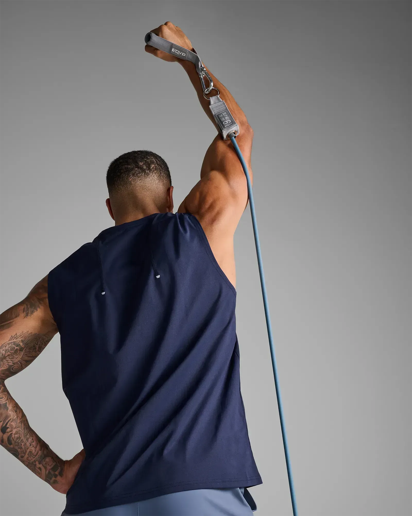 Man performing a standing unilateral overhead press using EQYP Power Tube 70 lbs blue resistance tube, rear view
