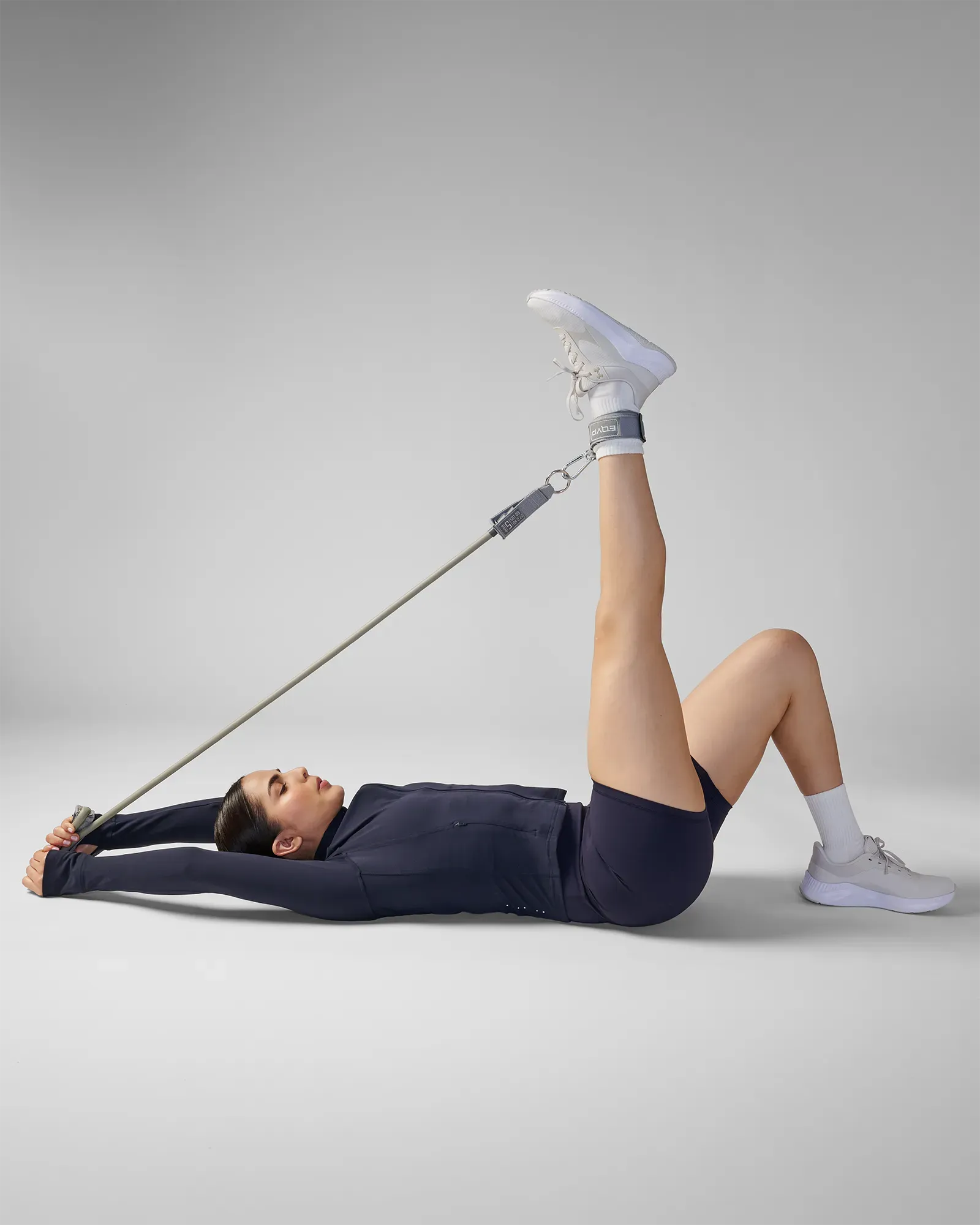 Woman performing a supine single-leg raise with ankle strap using EQYP Power Tube Extra Heavy gray resistance tube