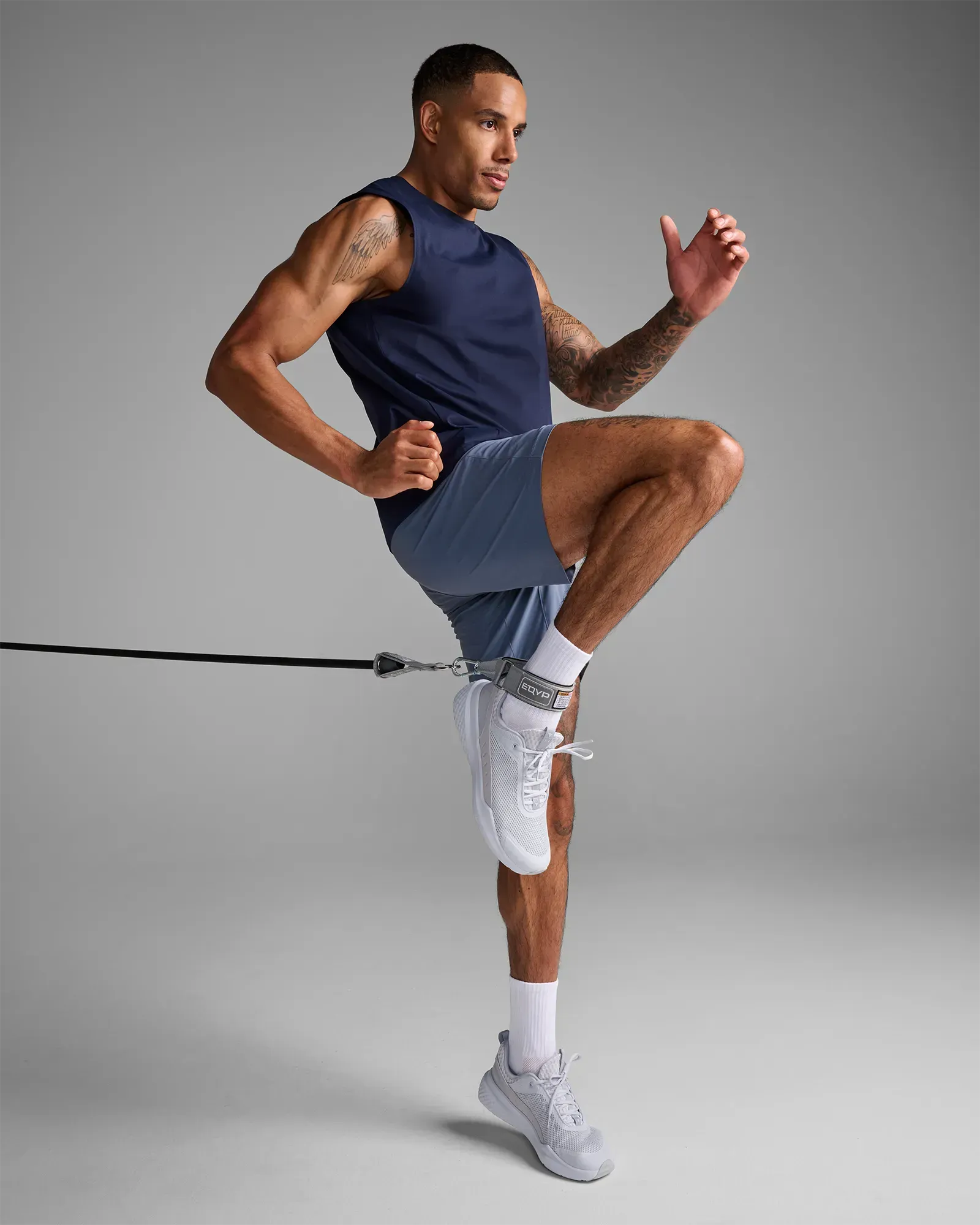 Man performing a standing high knee drive using the EQYP Power Tubes Ankle Strap attached to a resistance tube