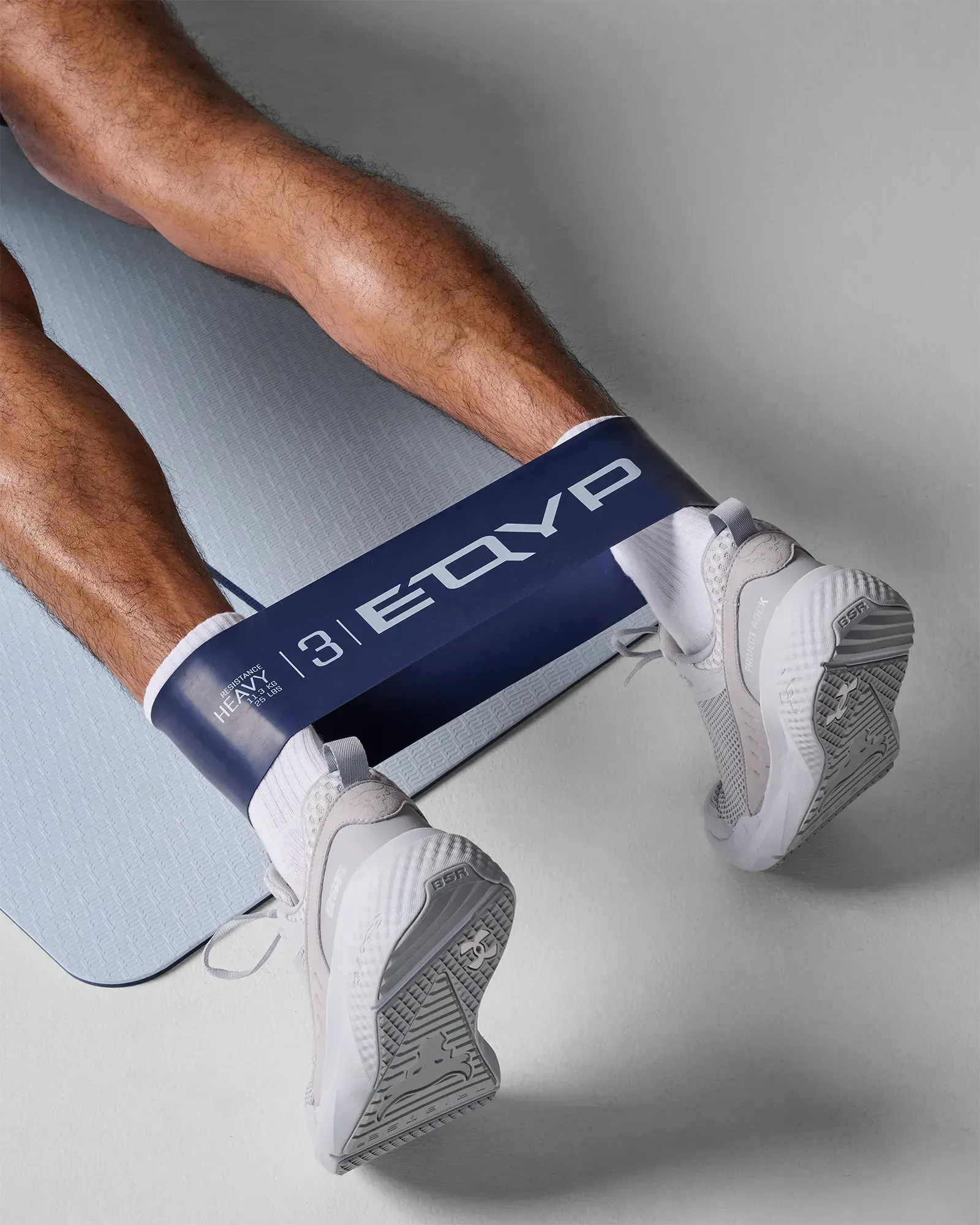 Close-up of man performing a seated bilateral leg press stretch using EQYP Ultimate Power Loop Heavy navy resistance band around the ankles on a yoga mat
