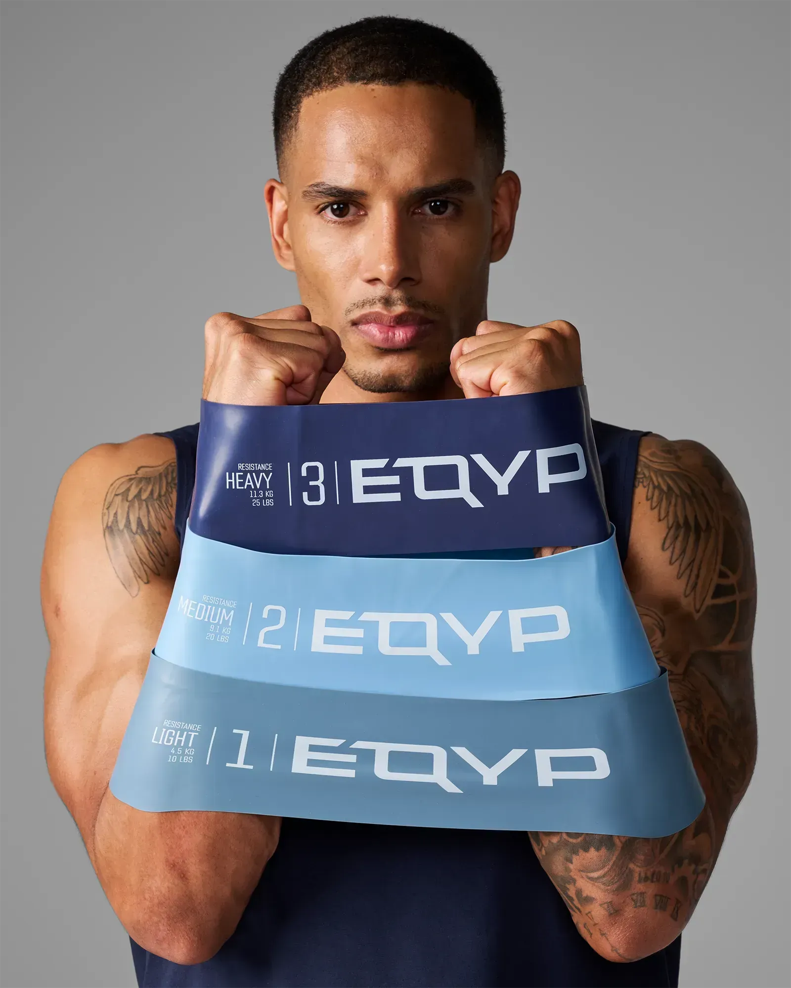 Man holding all three EQYP Ultimate Power Loops showing Light 10 lbs slate blue, Medium 20 lbs light blue, and Heavy 25 lbs navy resistance bands