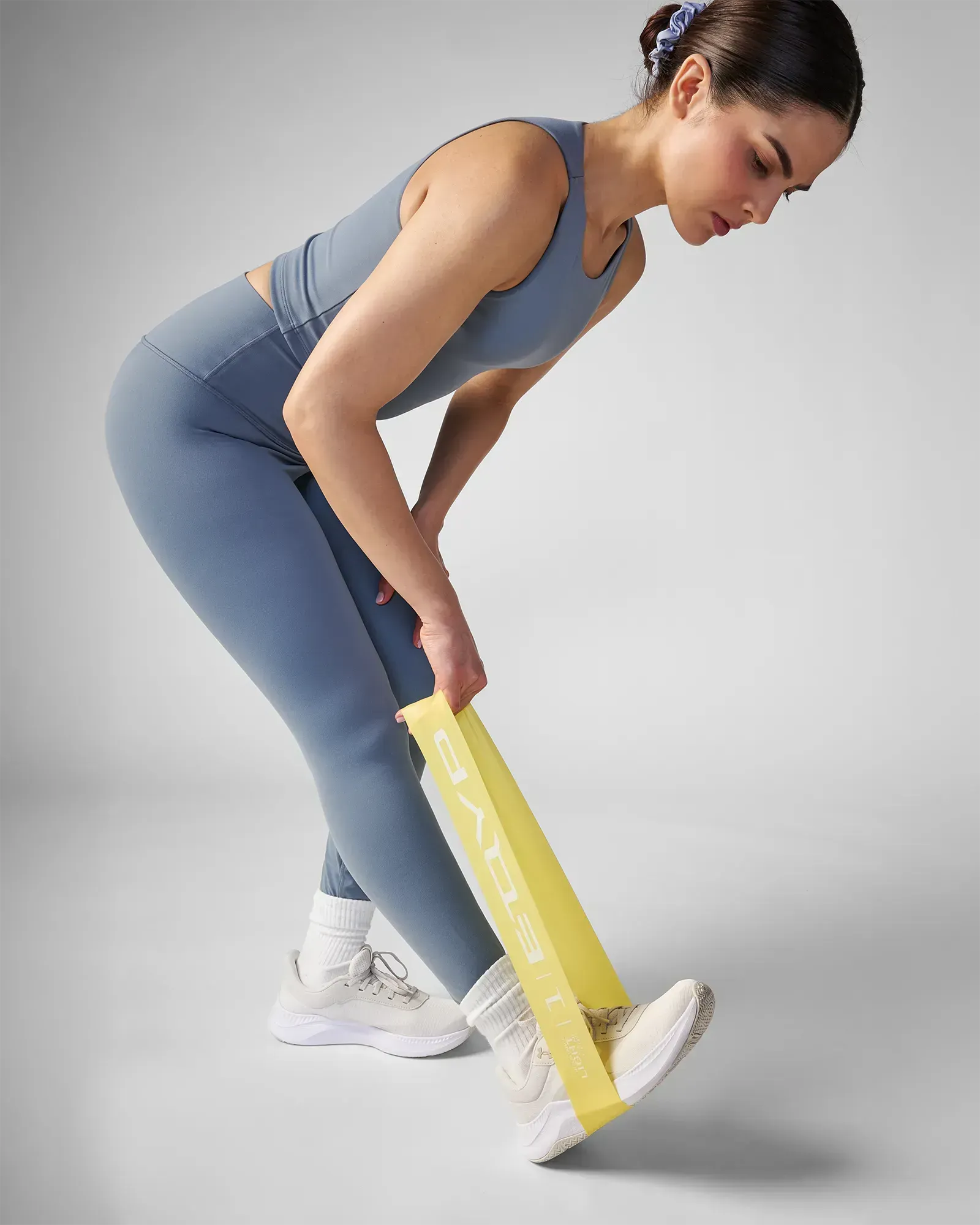 Woman performing a standing unilateral assisted hamstring stretch using EQYP Advanced Power Loop Light yellow resistance band looped around the foot
