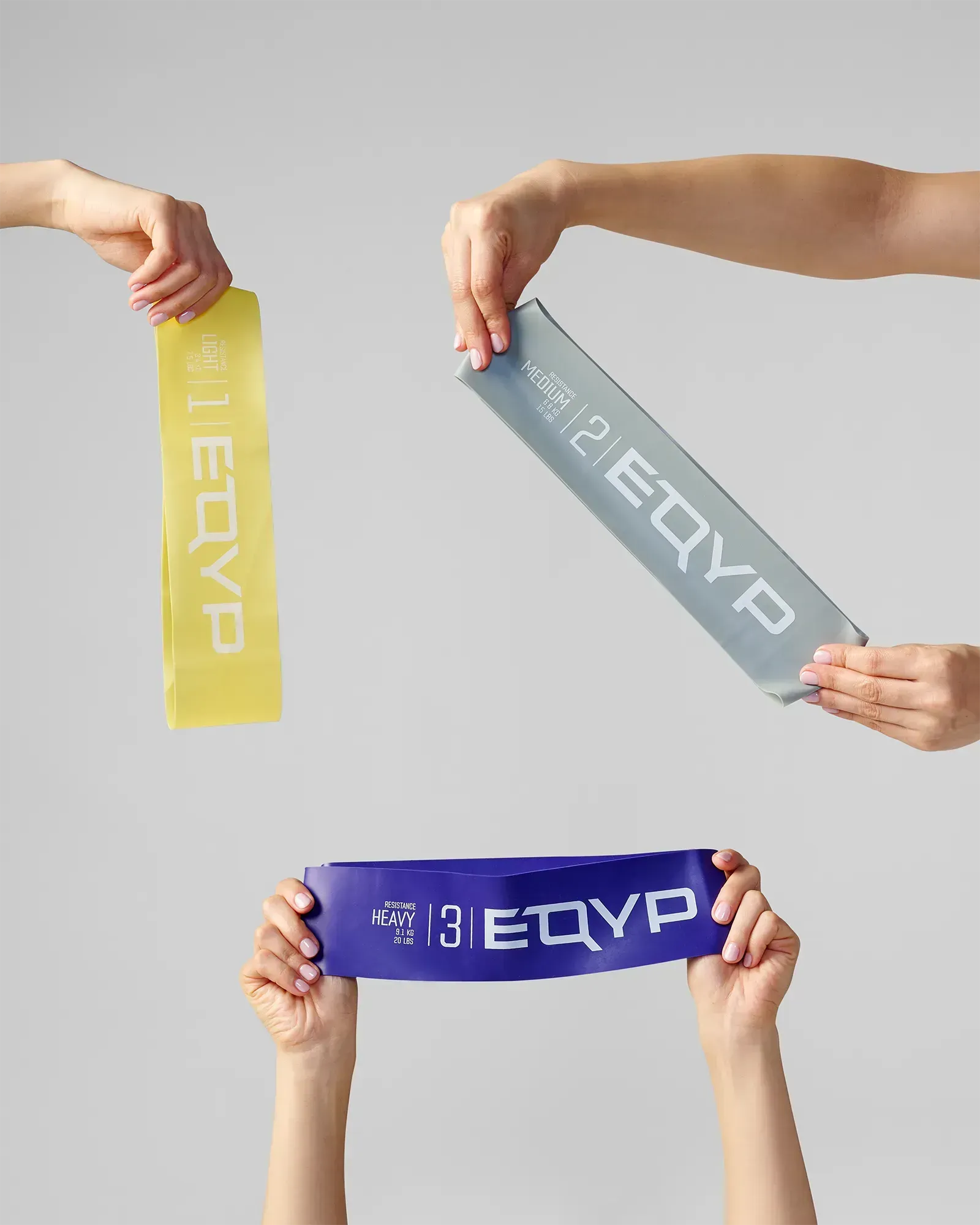 Three EQYP Advanced Power Loops held by hands showing Light yellow, Medium gray, and Heavy purple resistance bands