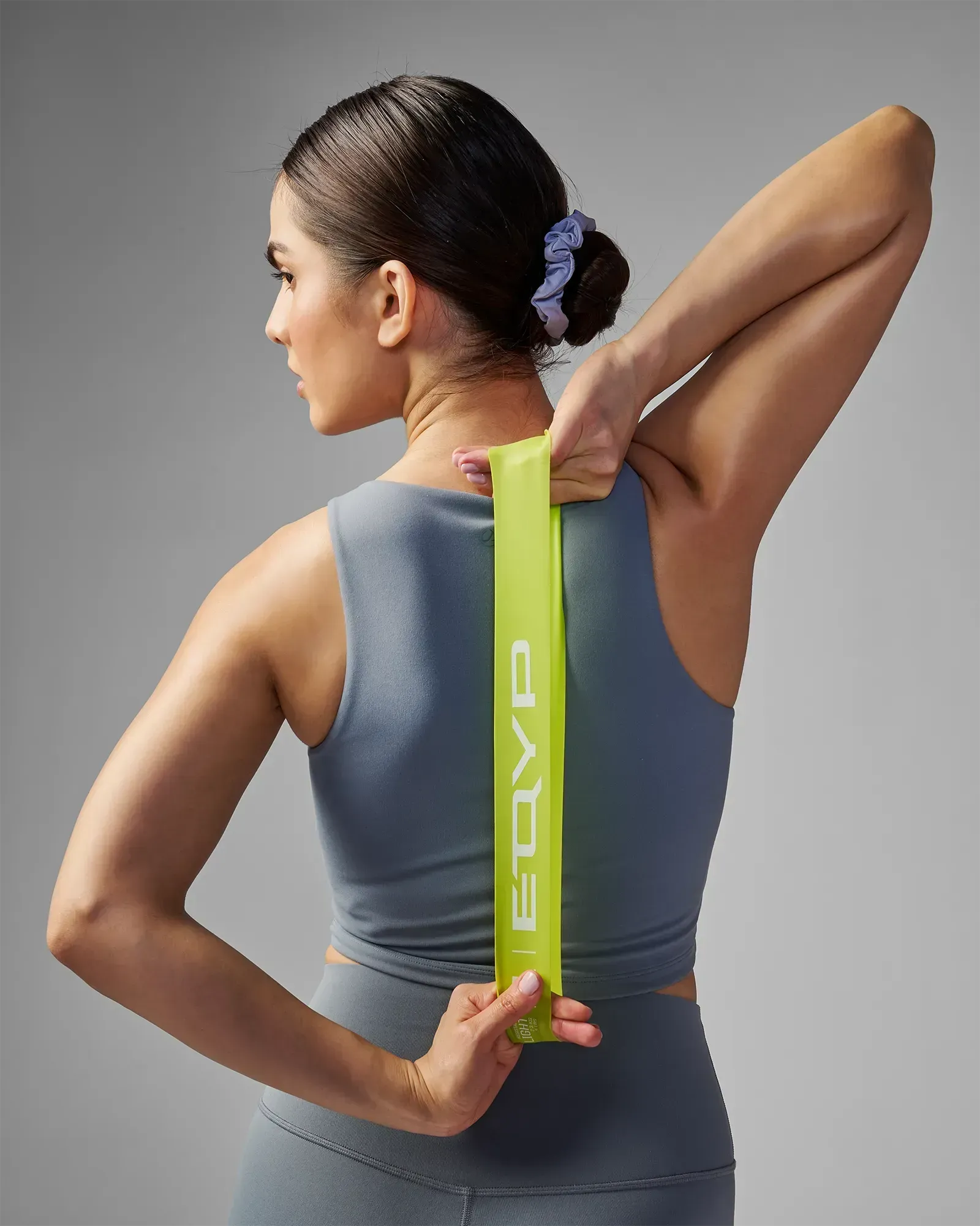 Woman performing a standing unilateral shoulder and tricep stretch using EQYP Power Loop Light yellow-green resistance band