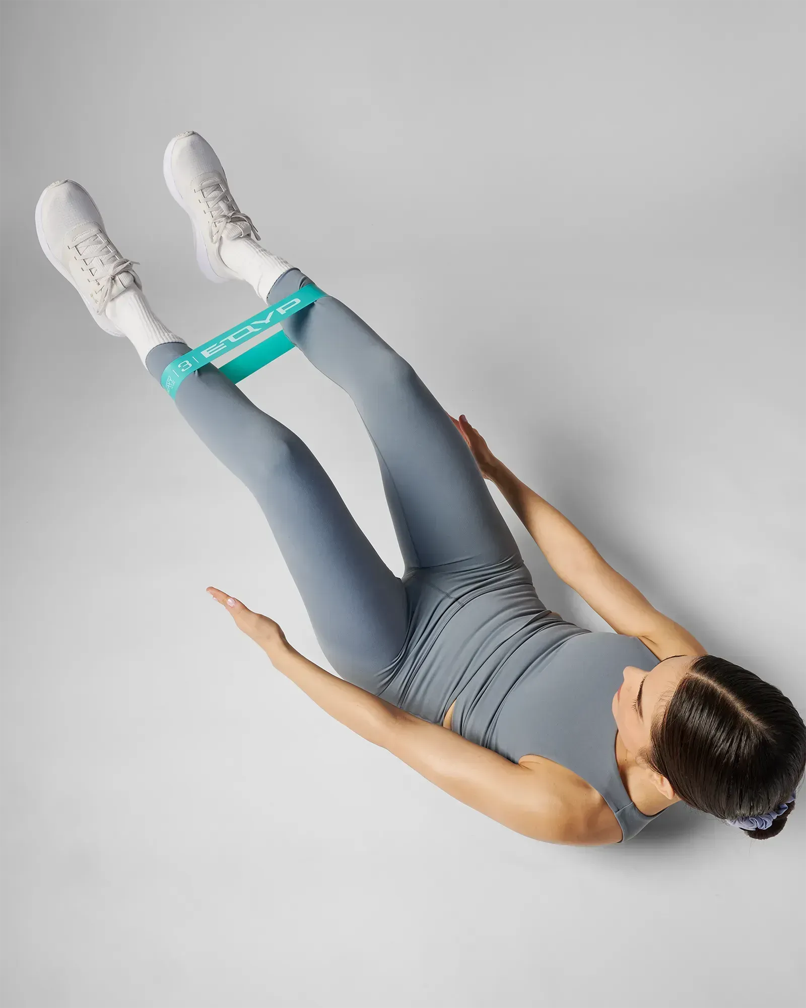Woman performing a supine bilateral leg raise using EQYP Power Loop Heavy teal resistance band above the knees