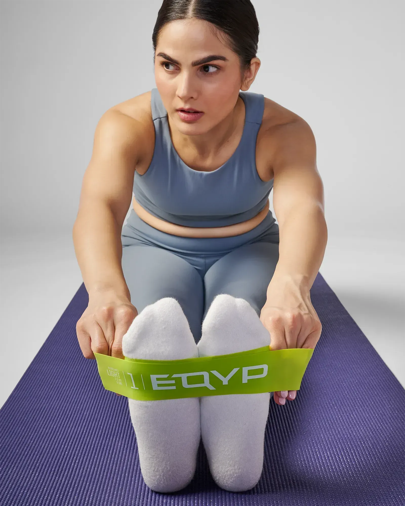 Woman performing a seated bilateral hamstring stretch on a yoga mat using EQYP Power Loop Light yellow-green resistance band around both feet