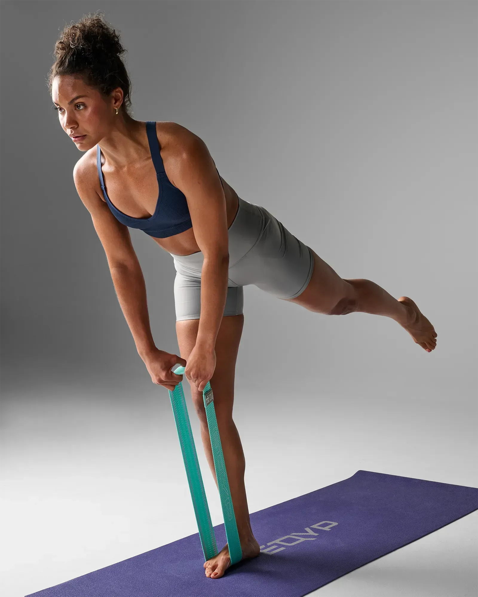 Woman performing a single-leg deadlift on a yoga mat using an EQYP teal elastic wide squat band