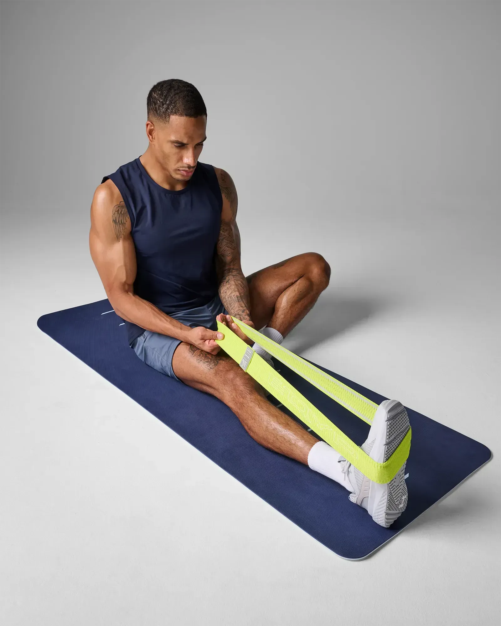 Man performing a seated ankle flex stretch on a yoga mat using an EQYP lime elastic wide squat band around his feet