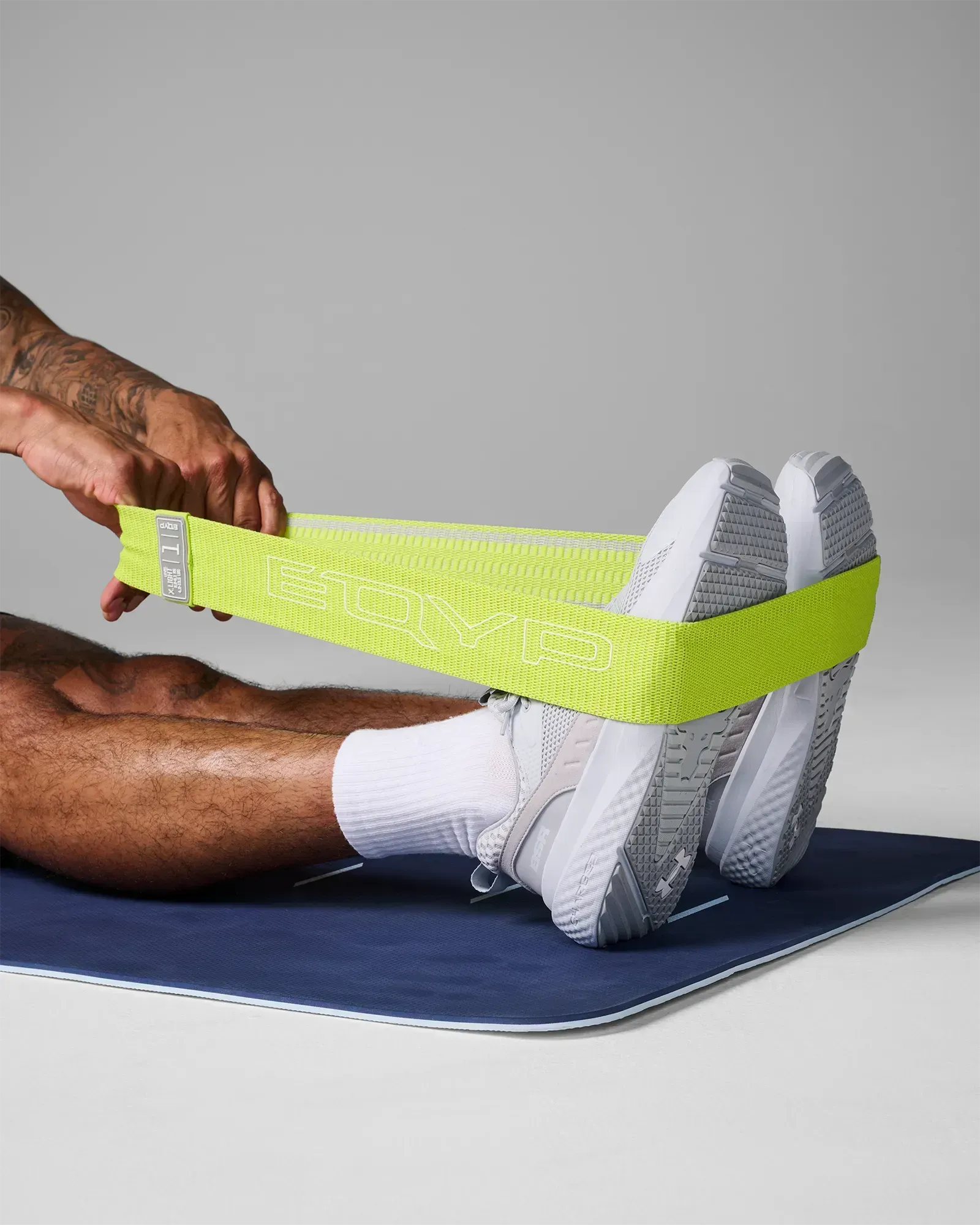 Man performing a supine leg press stretch on a yoga mat using an EQYP lime elastic wide squat band around his feet