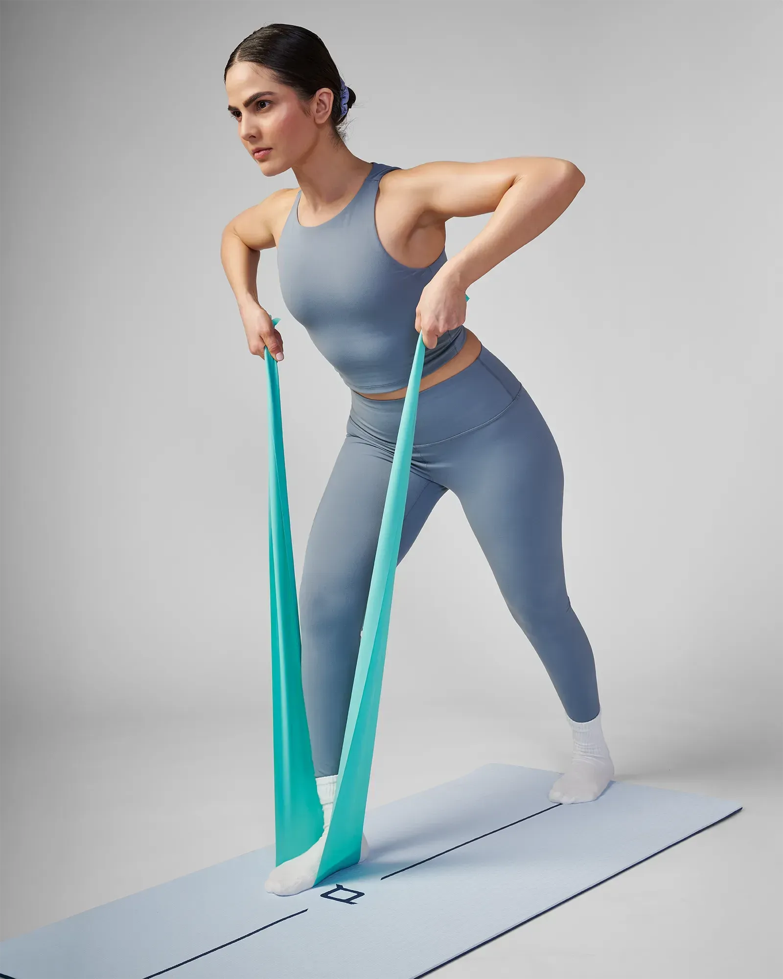 Woman performing a standing bent-over row on a yoga mat using an EQYP turquoise latex-free flat resistance band