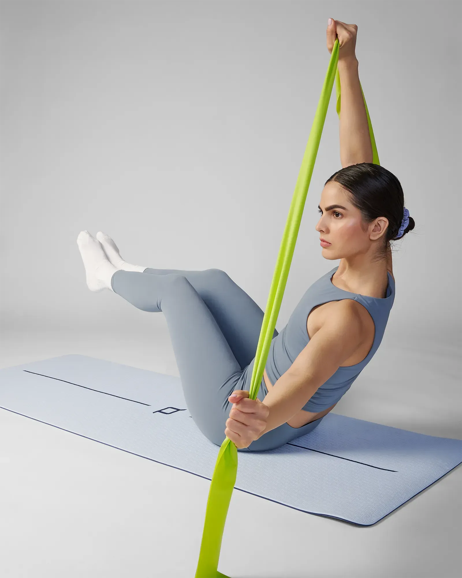 Woman performing a seated Pilates stretch on a yoga mat using an EQYP green latex-free flat resistance band