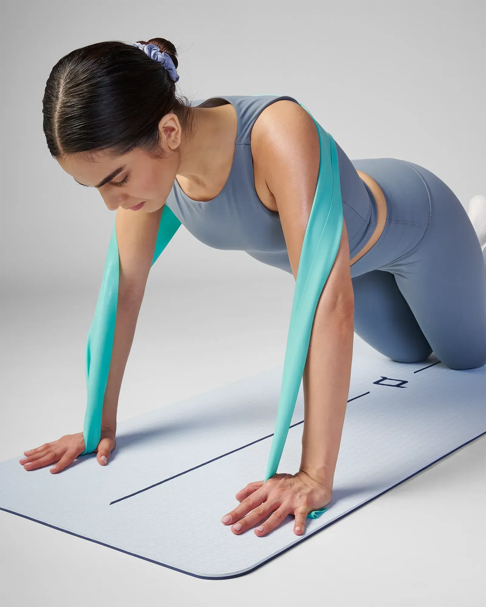 Woman using a resistance band on a yoga mat with a plain background