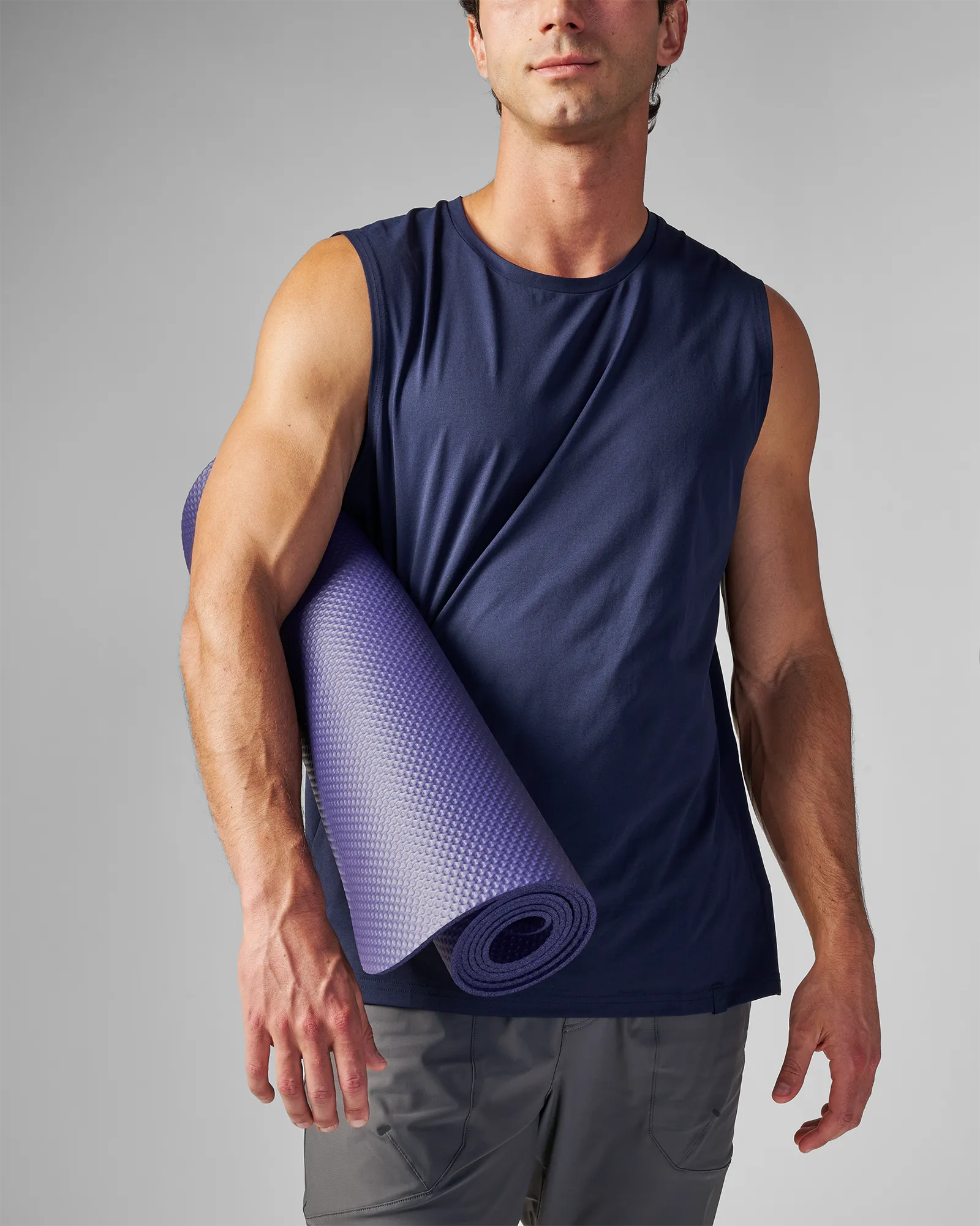 Man carrying a rolled EQYP Yoga Mat in navy blue under his arm showing the textured grip surface