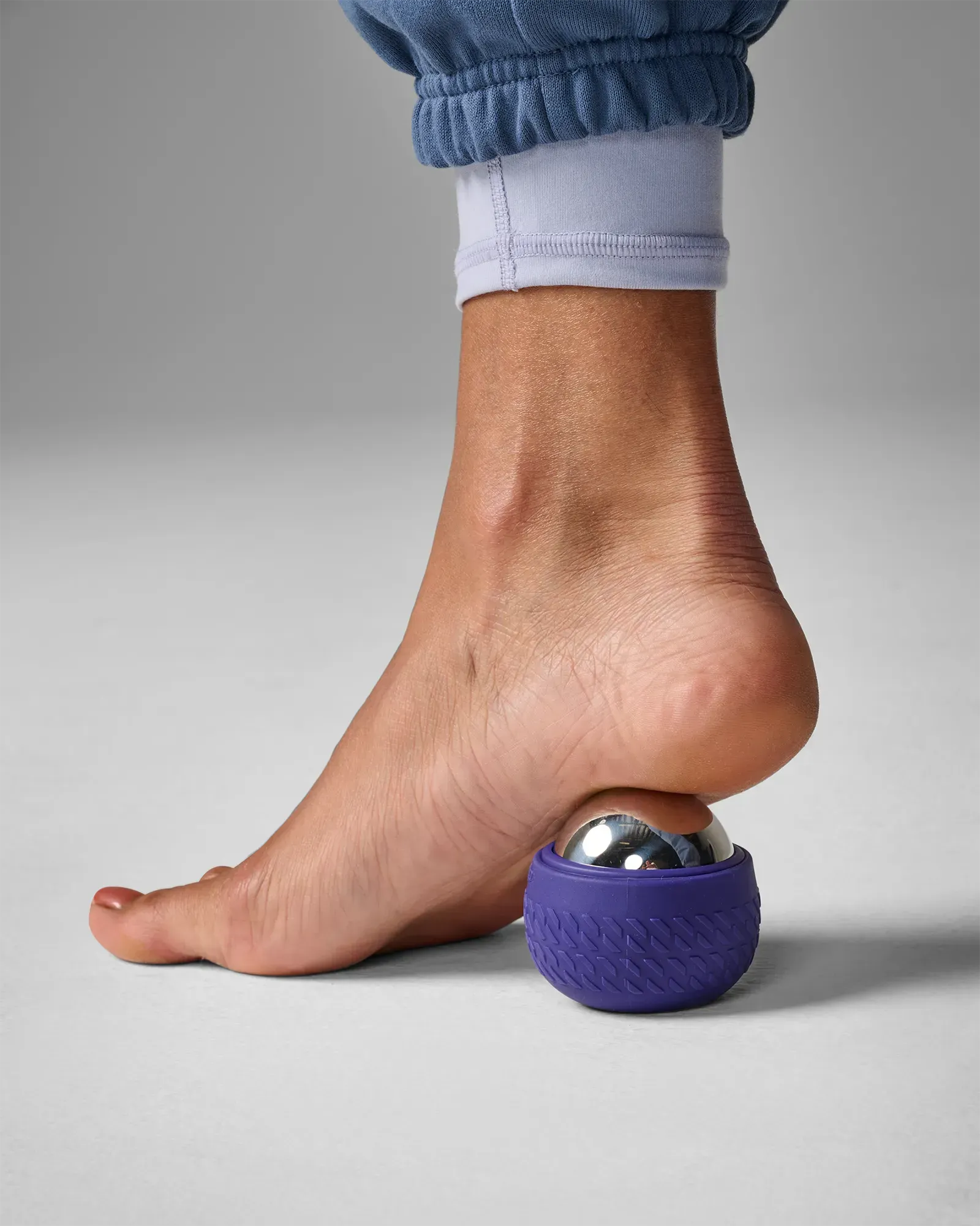 Woman using stainless steel core EQYP roll-on massager with textured outer shell on foot