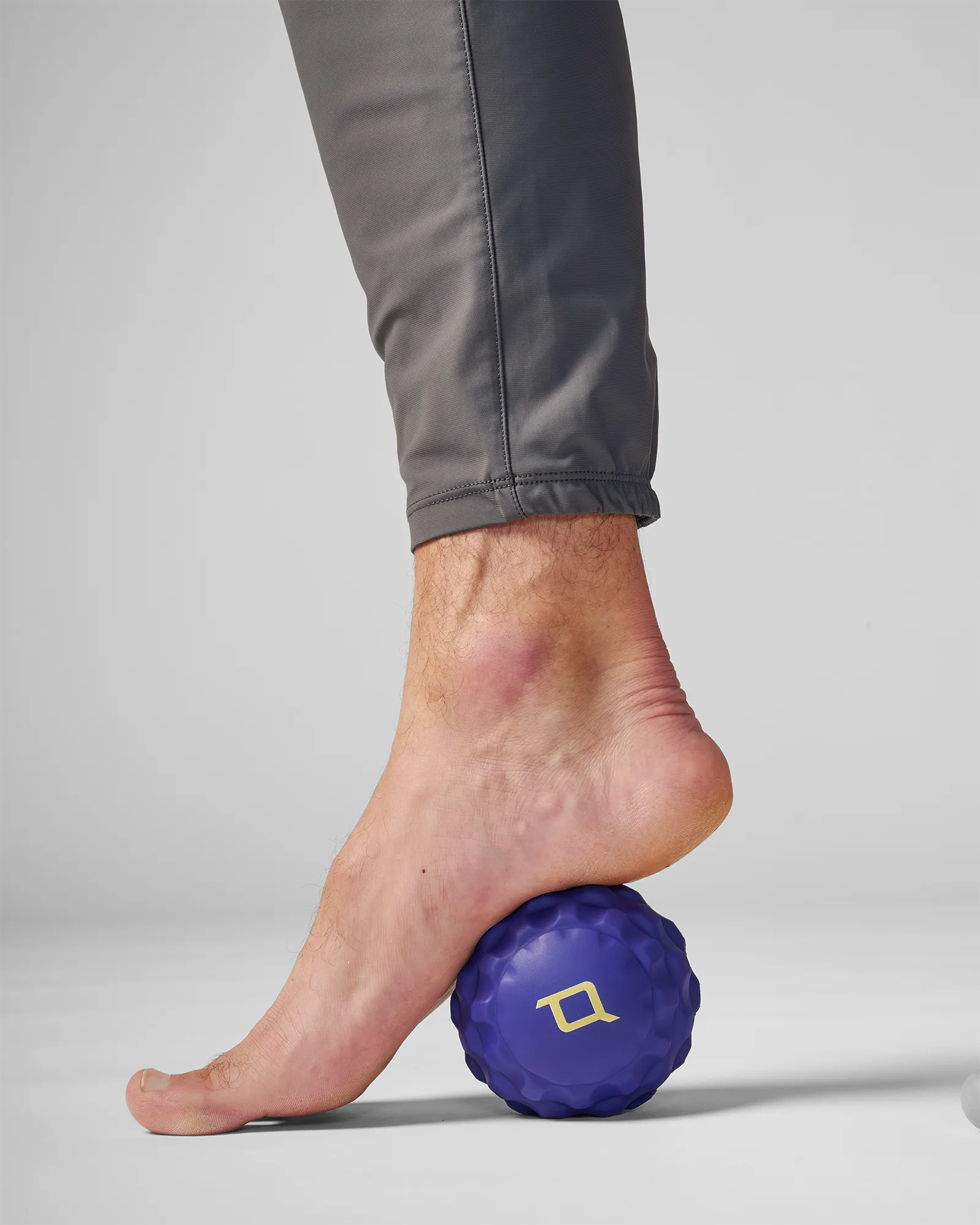Man rolling medium sized blue EQYP massage ball on back part of foot for muscle relief