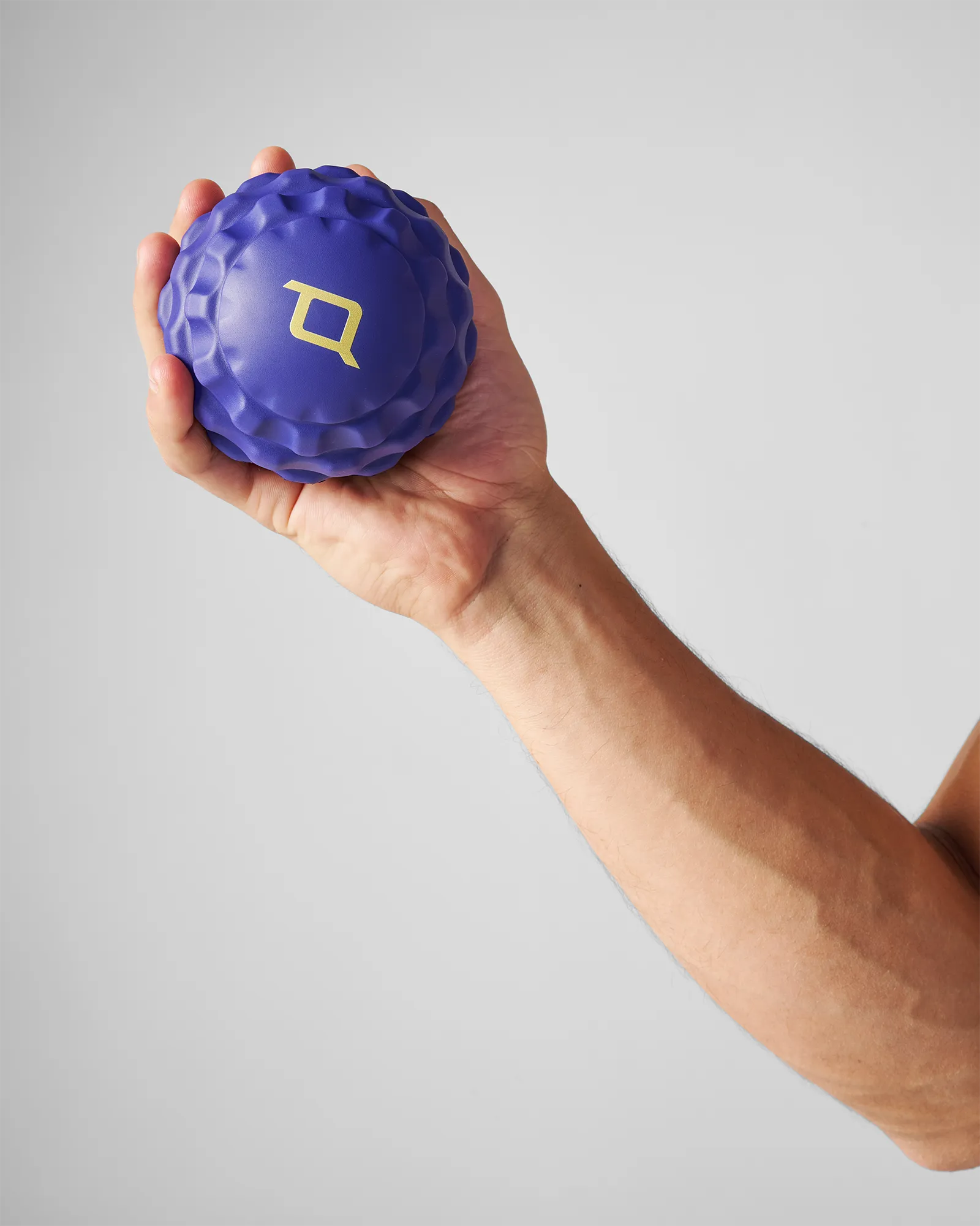 Hand holding medium sized blue EQYP textured massage ball for muscle relief