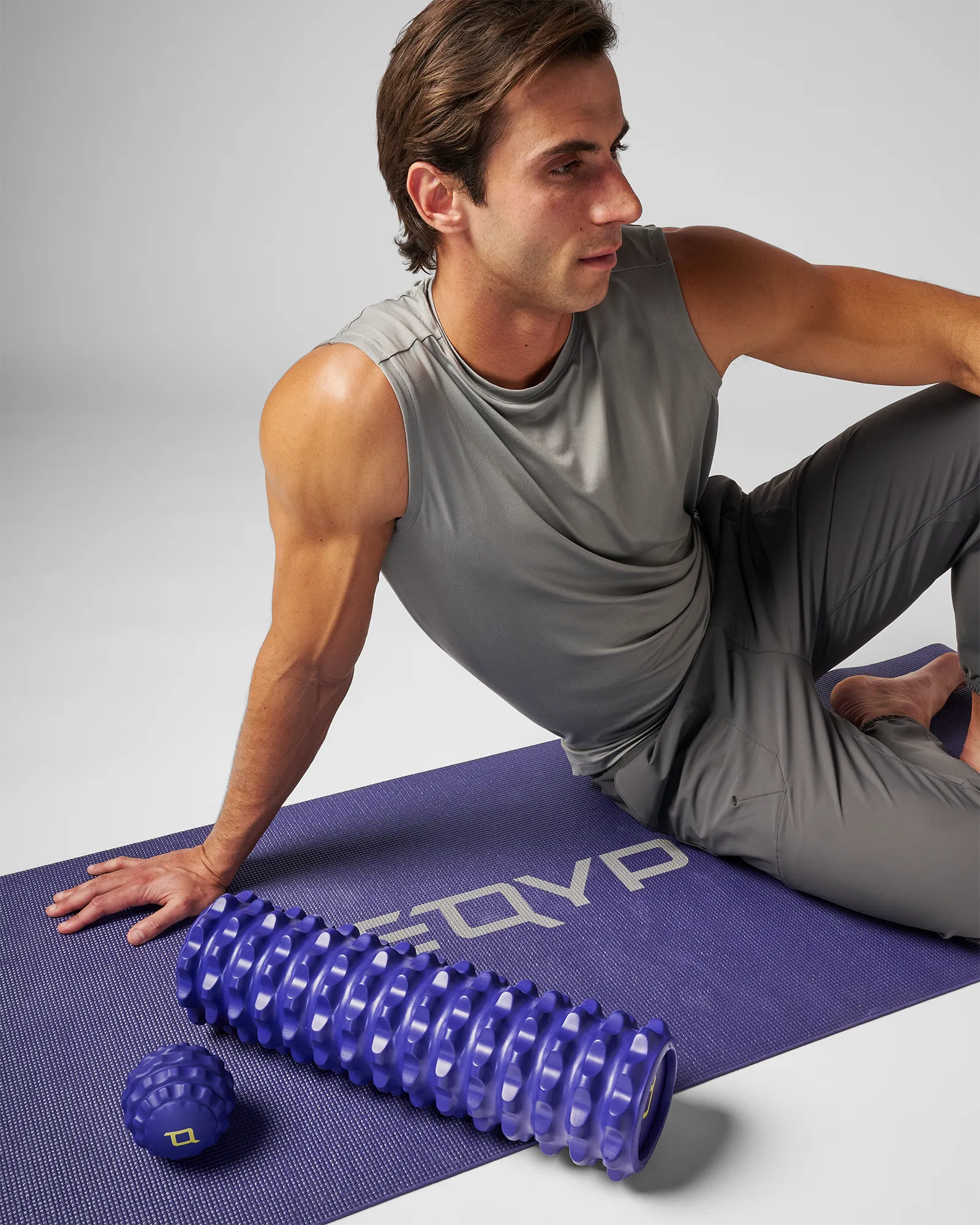 Man sitting on yoga mat next to medium sized blue EQYP massage ball