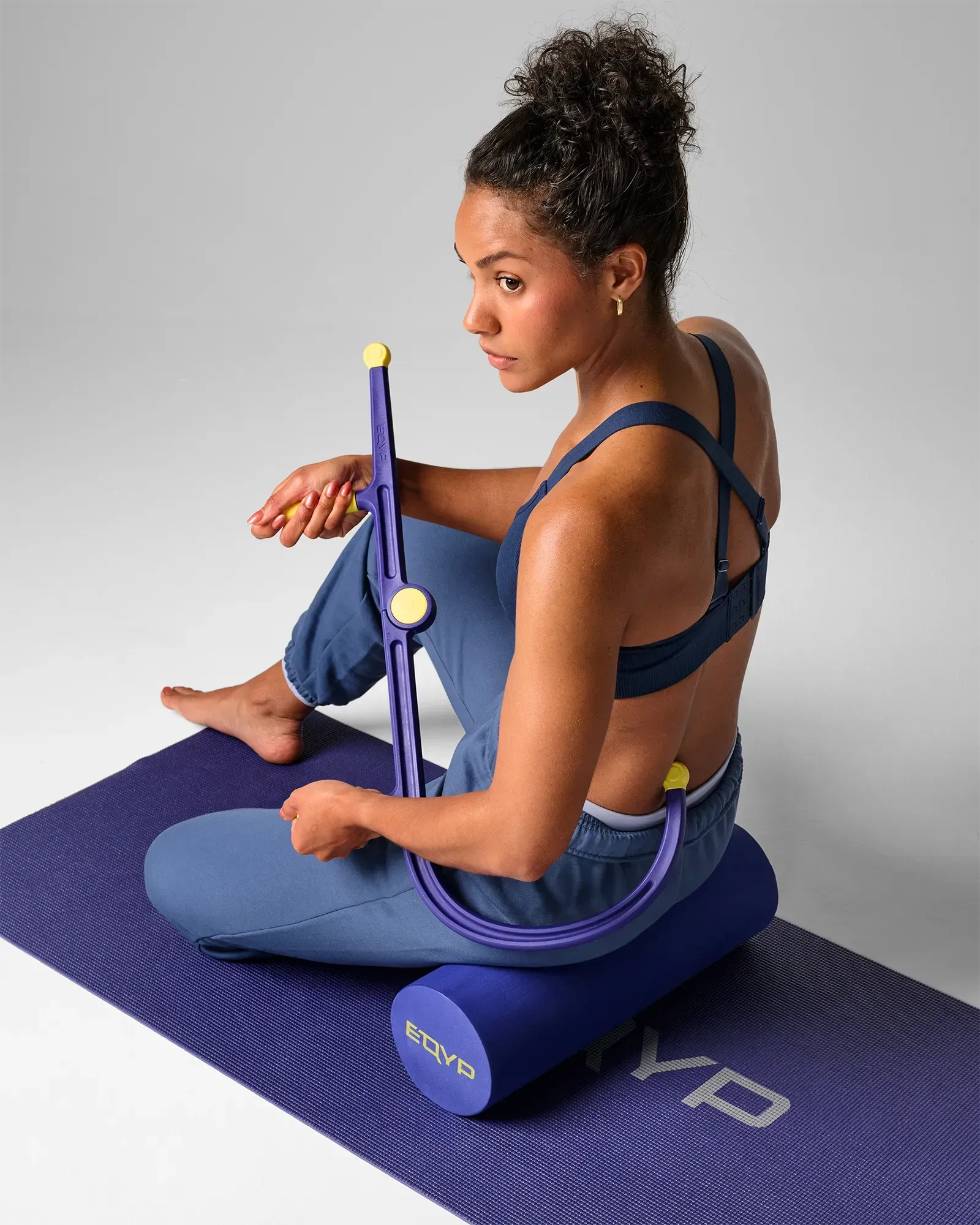 Woman on exercise mat using muscle hook recovery massager tool on lower back