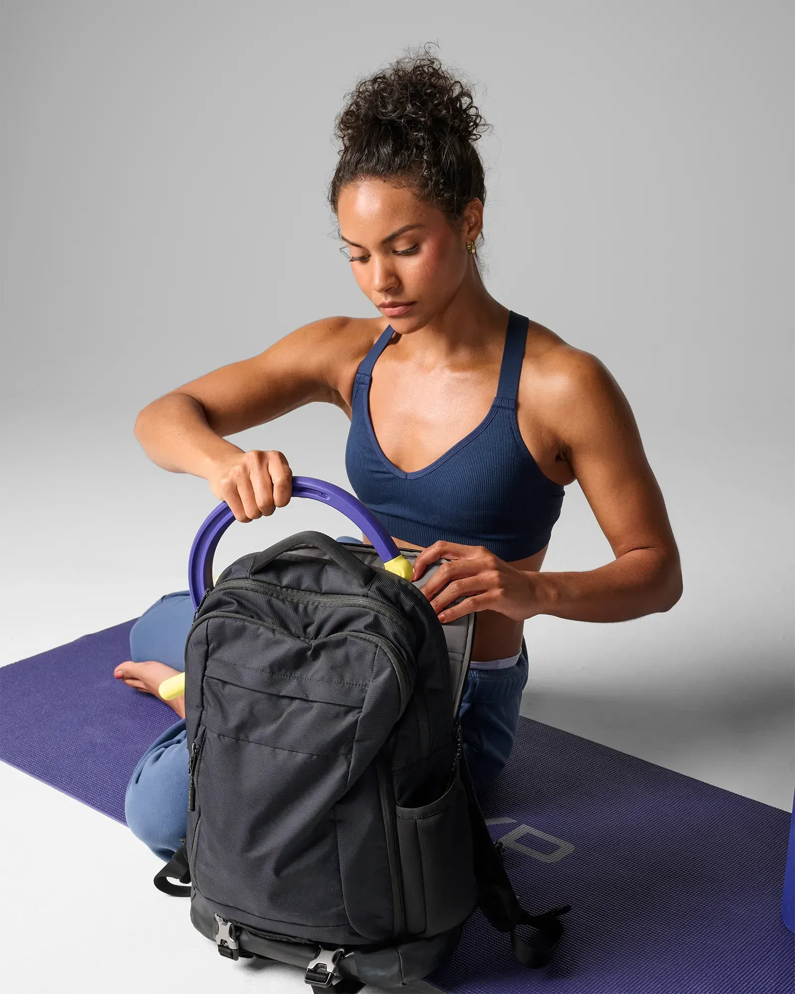 Woman on exercise mat putting folded muscle hook recovery massager tool in backpack