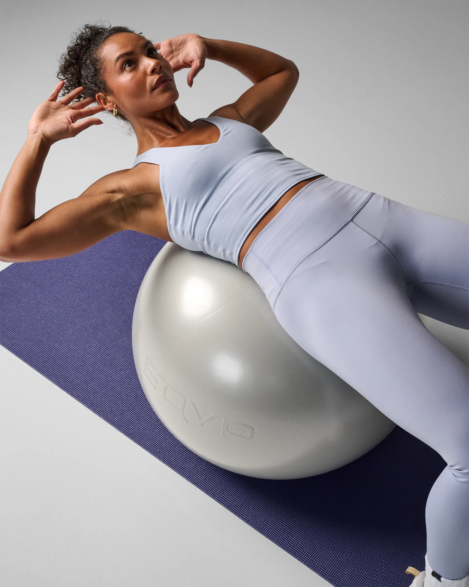 Woman performing a stability ball oblique crunch on a yoga mat using an EQYP Pro Stability Ball 55cm in pearl white with lower back supported on the ball