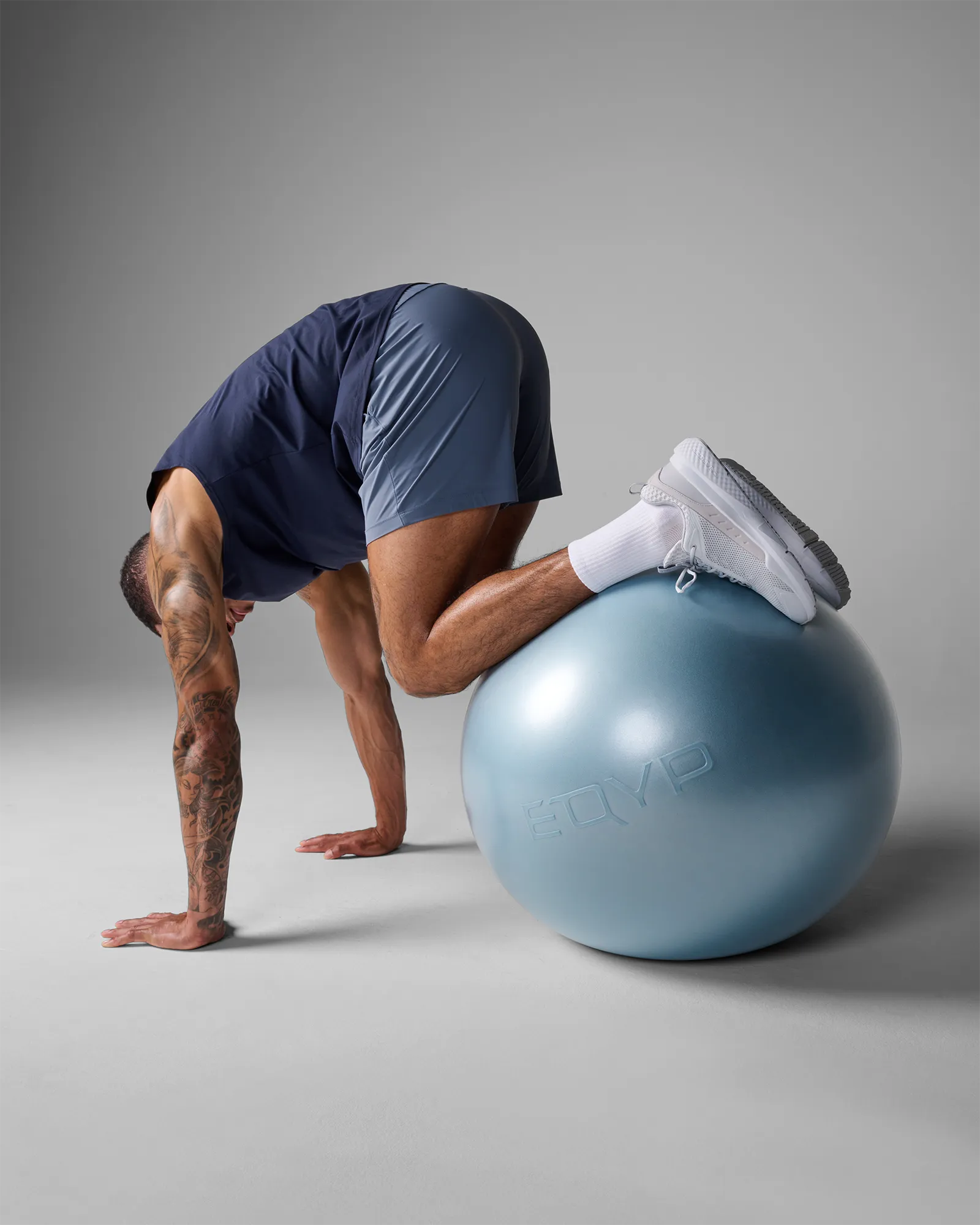 Man performing a stability ball tuck on an EQYP Pro Stability Ball 65cm with knees drawn toward chest and hands on the floor