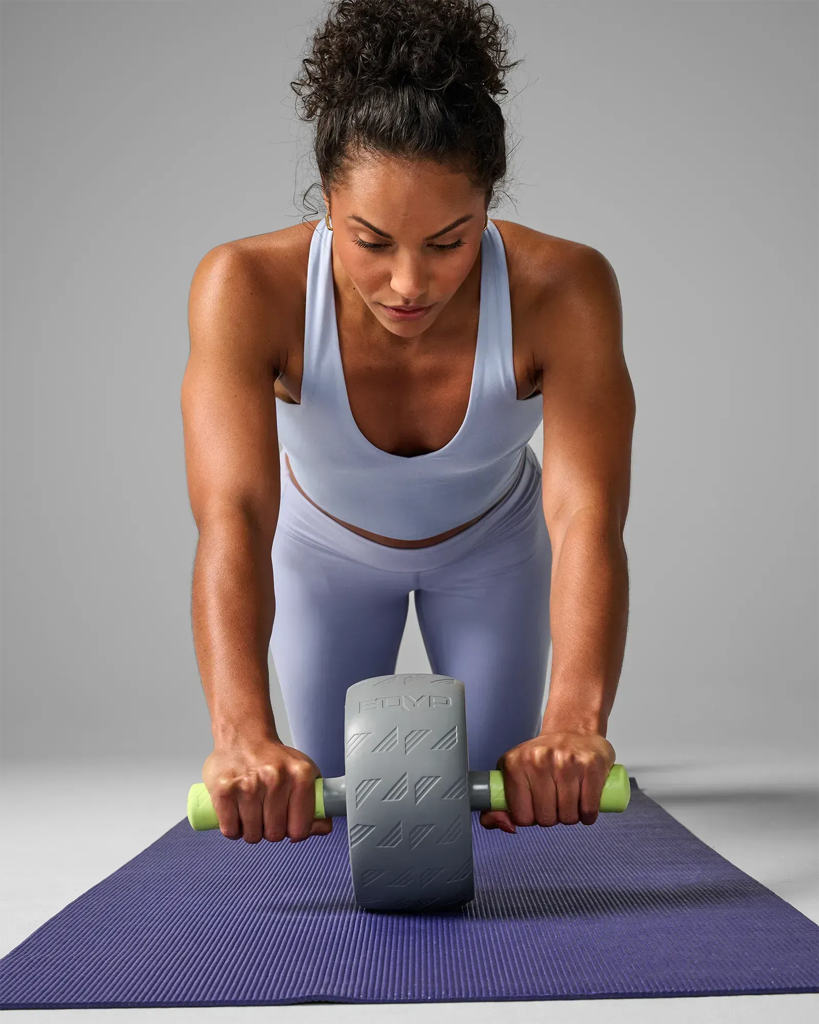 Woman performing a kneeling ab wheel rollout on a yoga mat using the EQYP Q-Tech Ab Wheel with gray wheel and neon green handles, front view