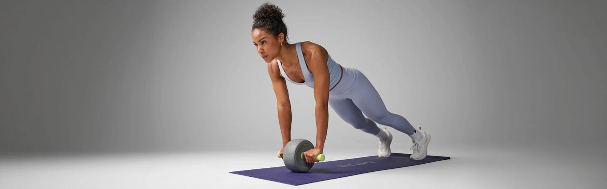 Woman in a plank position rolling an EQYP Ab Wheel across a yoga mat during a core workout.