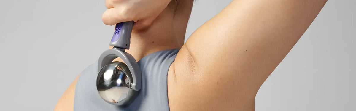 Close-up of a person applying a metal EQYP cold therapy roller ball to the back of their neck and shoulder.