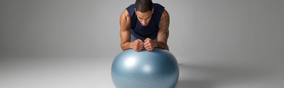 Man leaning forward with his fists resting on a blue EQYP Stability Ball during a core exercise.
