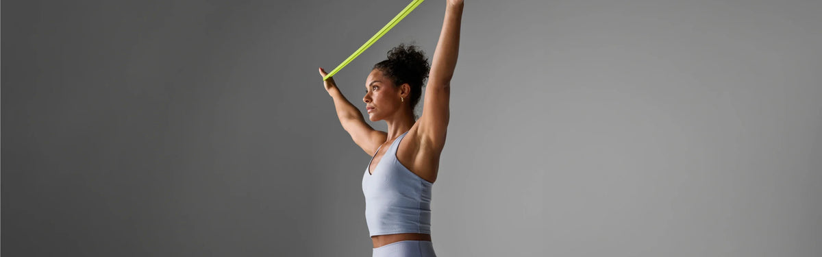 Woman stretching a yellow-green EQYP super band overhead with both arms raised