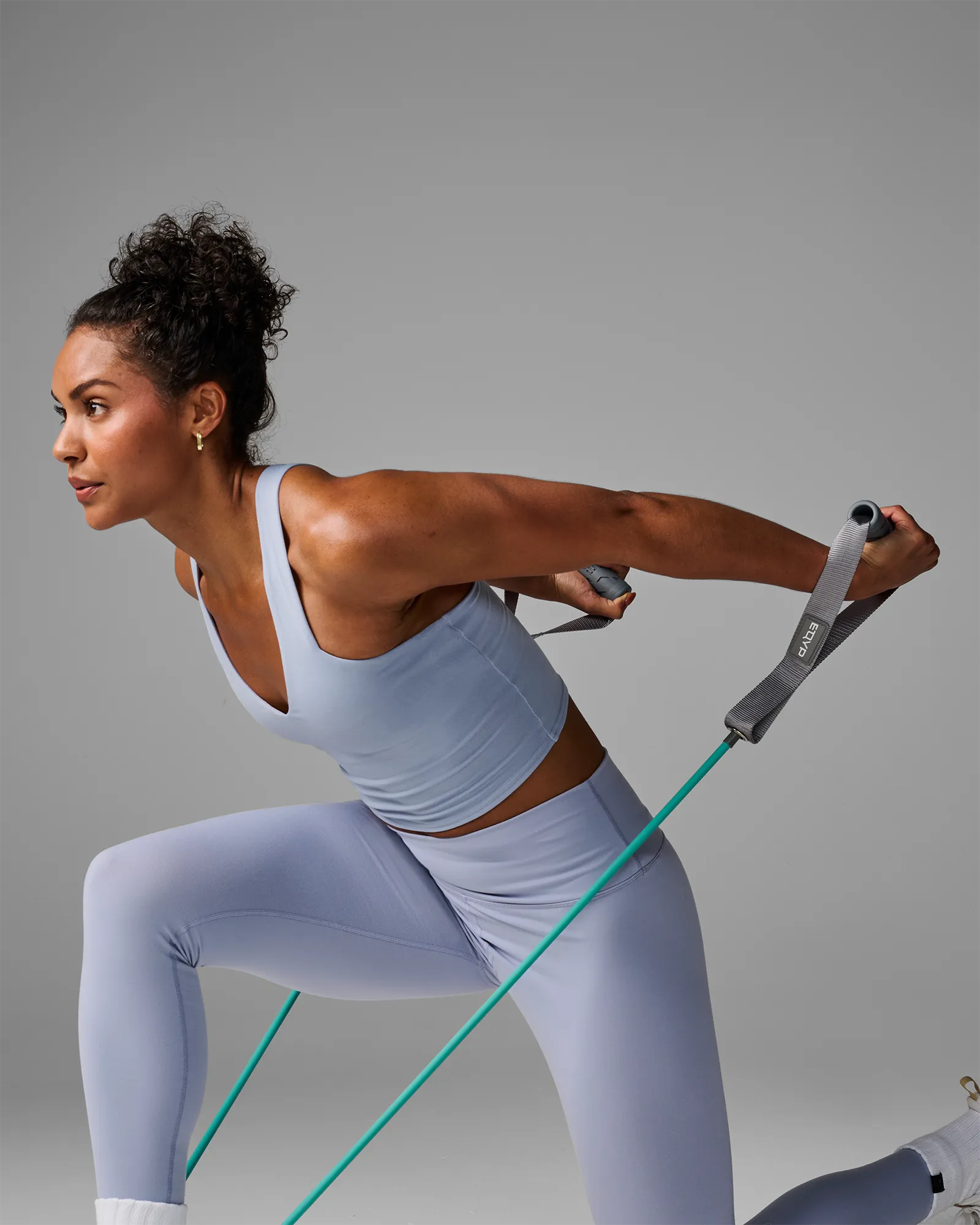 Woman performing a forward lunge with a bilateral triceps extension using EQYP Power Tubes with Handles turquoise resistance tube
