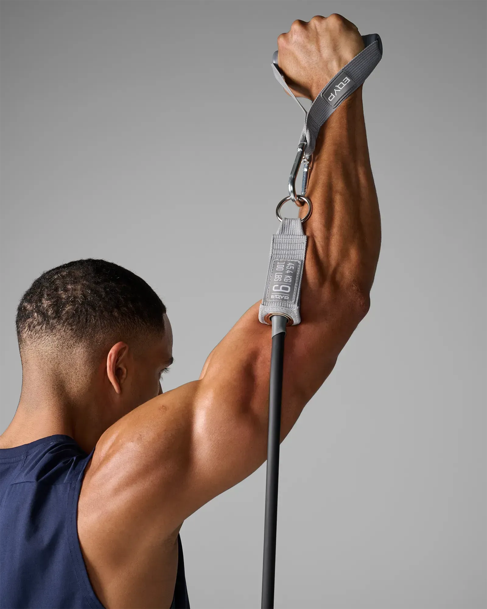 Man performing a standing single-arm overhead press using EQYP Power Tubes 100 lbs black resistance tube, rear view showing handle and carabiner detail