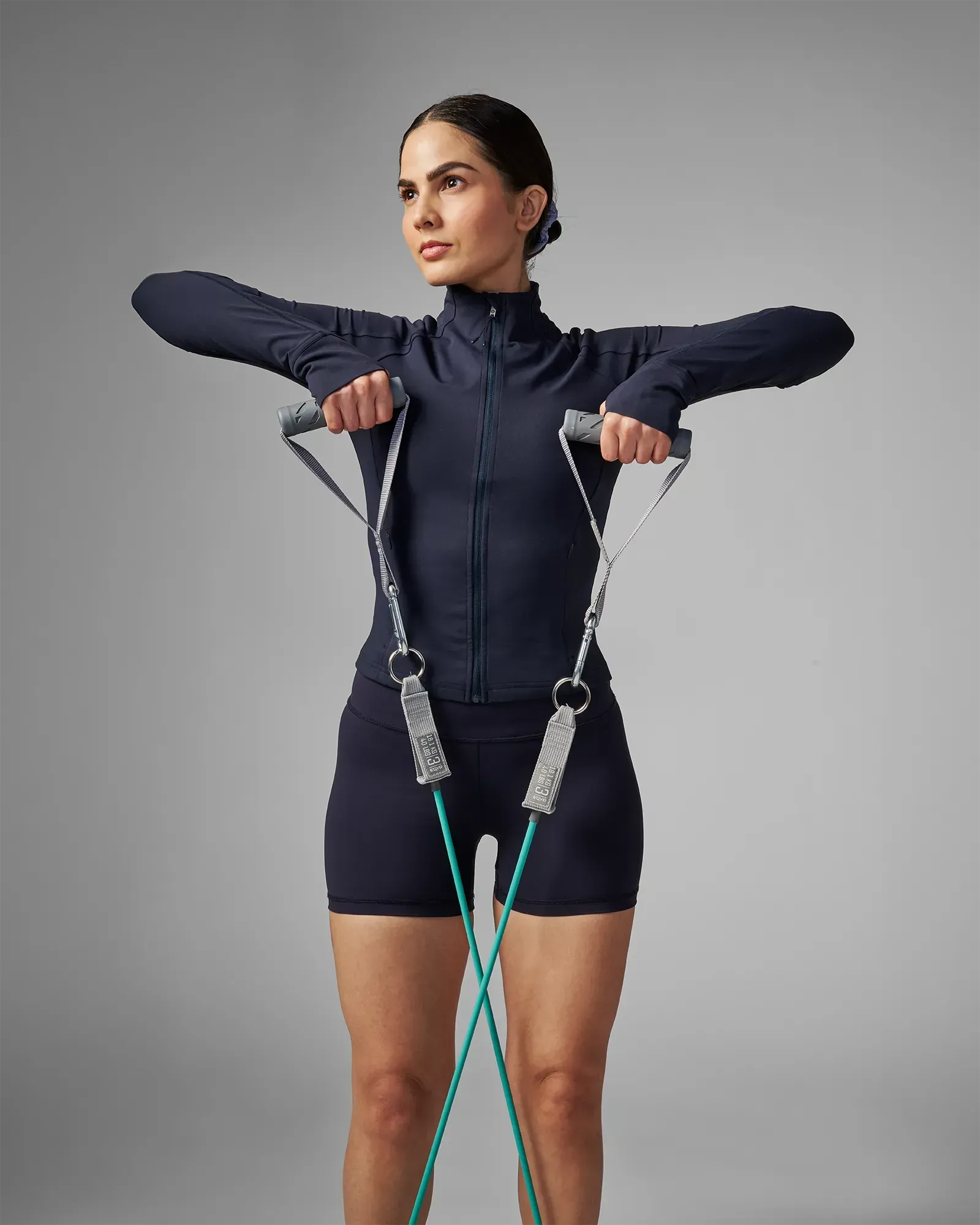 Woman performing a standing bilateral upright row using EQYP Power Tubes 40 lbs teal resistance tube with handles, front view
