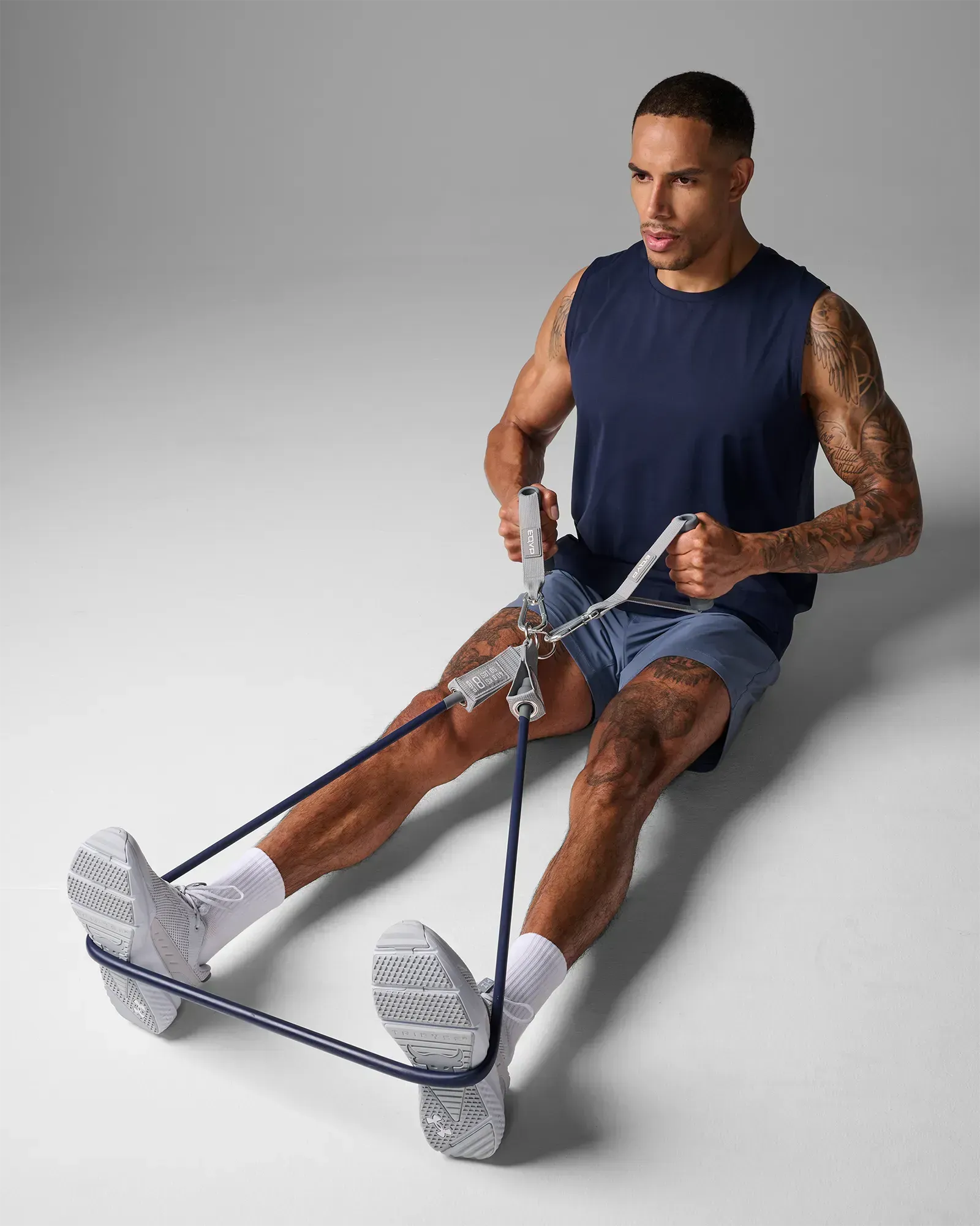 Man performing a seated bilateral cross row with feet braced using EQYP Power Tubes 90 lbs navy blue resistance tube with handles, three-quarter view