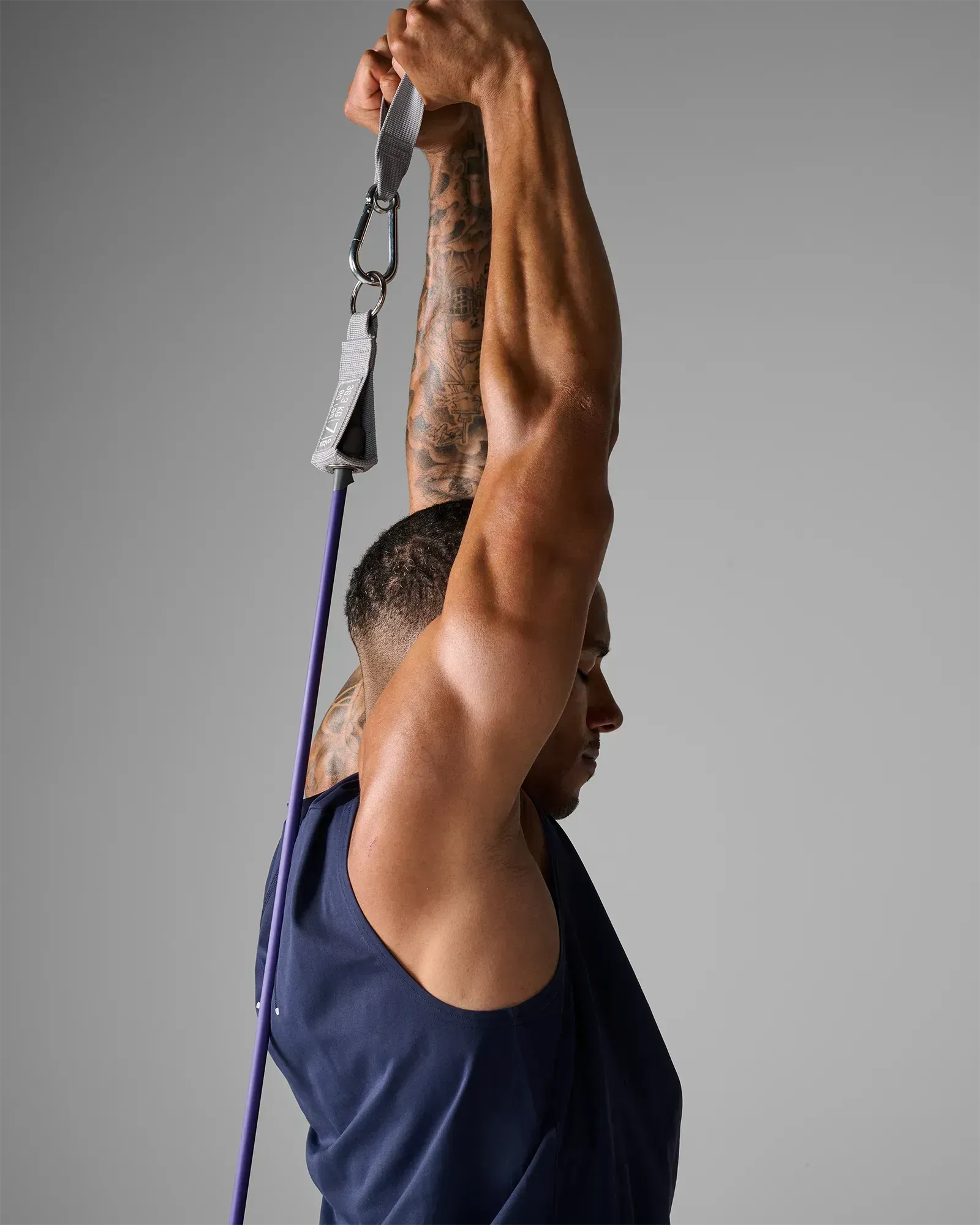 Man performing a standing unilateral overhead press using EQYP Power Tube 80 lbs purple resistance tube with gray handle, rear view