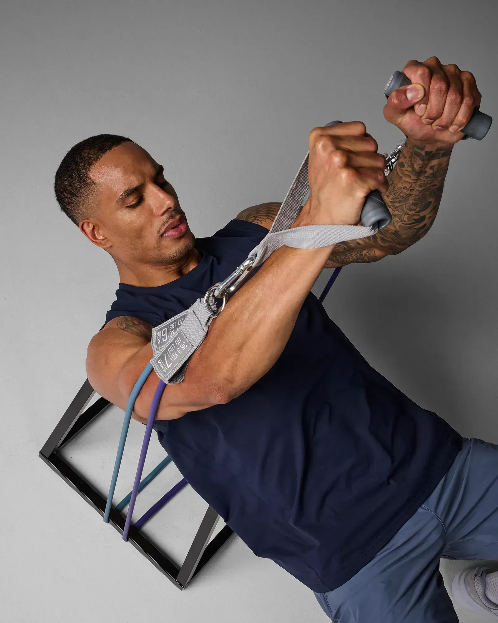Man performing a supine bilateral chest press on a bench using EQYP Power Tube 80 lbs purple resistance tube anchored at the base of the bench
