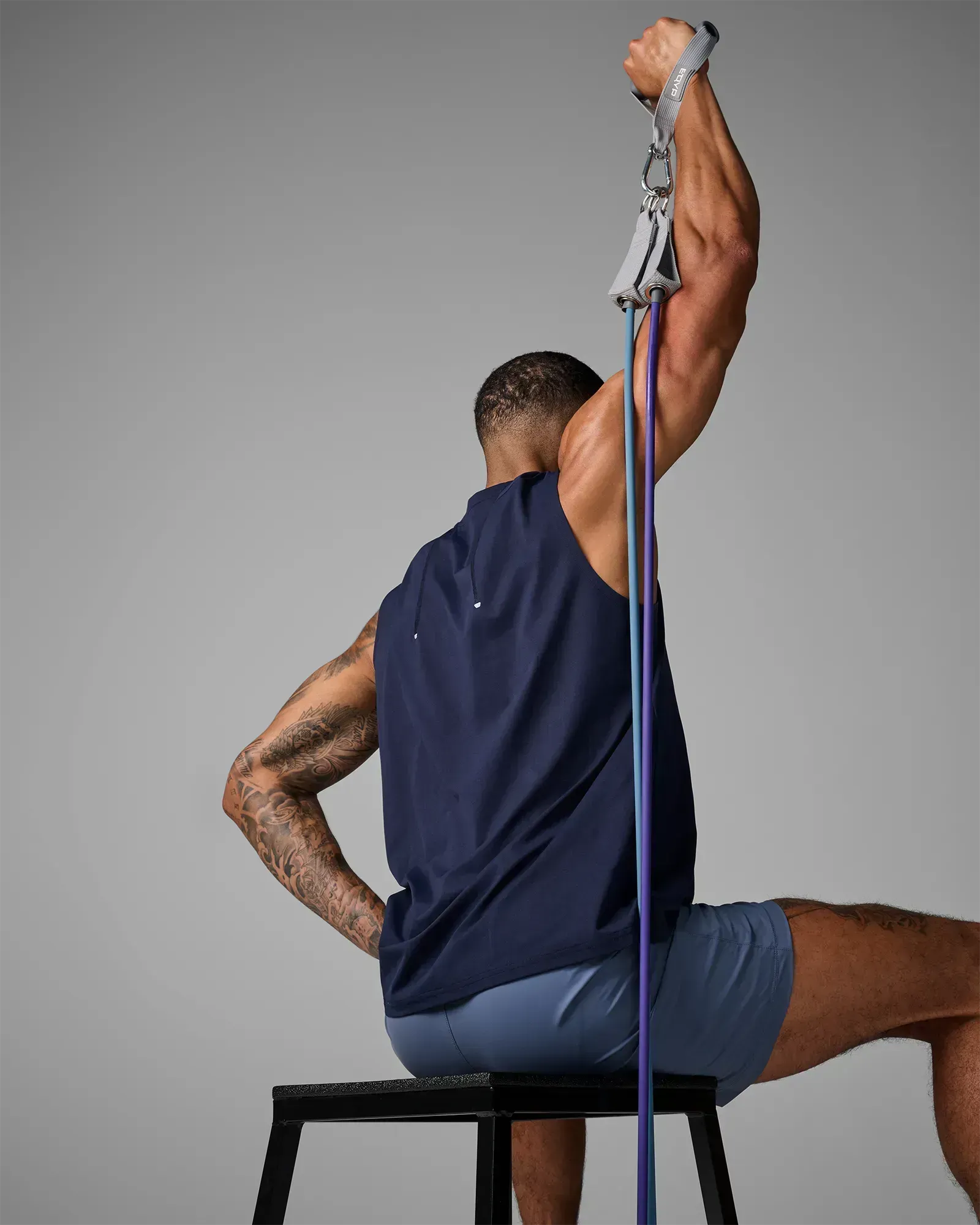 Man performing a seated unilateral overhead tricep extension using EQYP Power Tube 70 lbs blue resistance tube, rear view